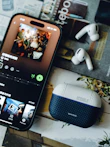 A smartphone playing music with wireless earbuds and a case.