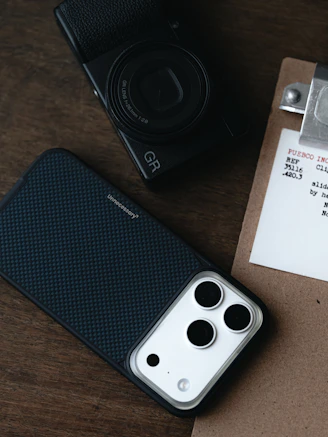 Smartphone case and digital camera on wooden table.