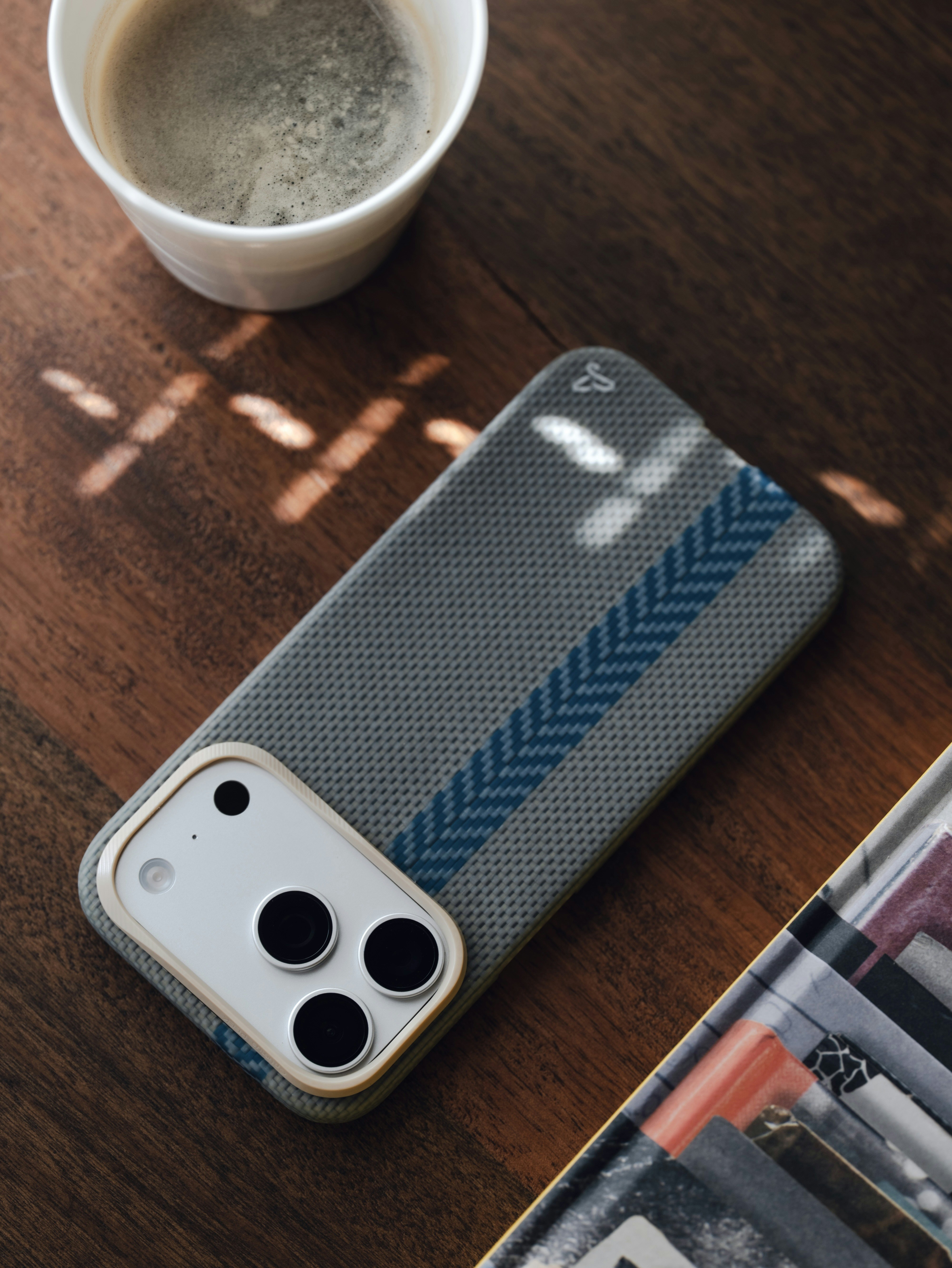 Smartphone con custodia a motivi, caffè e luce del sole su un tavolo di legno