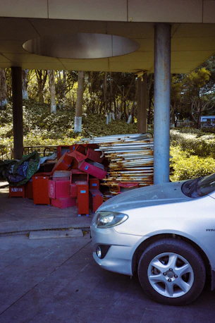 Silver car parked next to red bins and metal poles