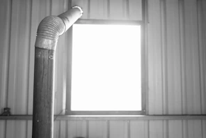 A pipe bends in front of a bright window.