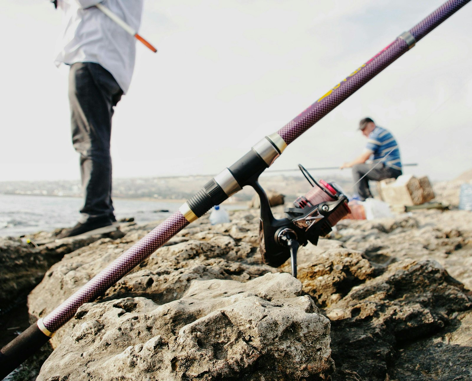Two anglers casting lines from a rocky saltwater shoreline