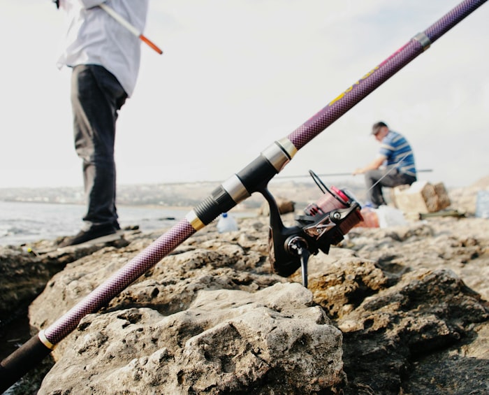 Two anglers casting lines from a rocky saltwater shoreline