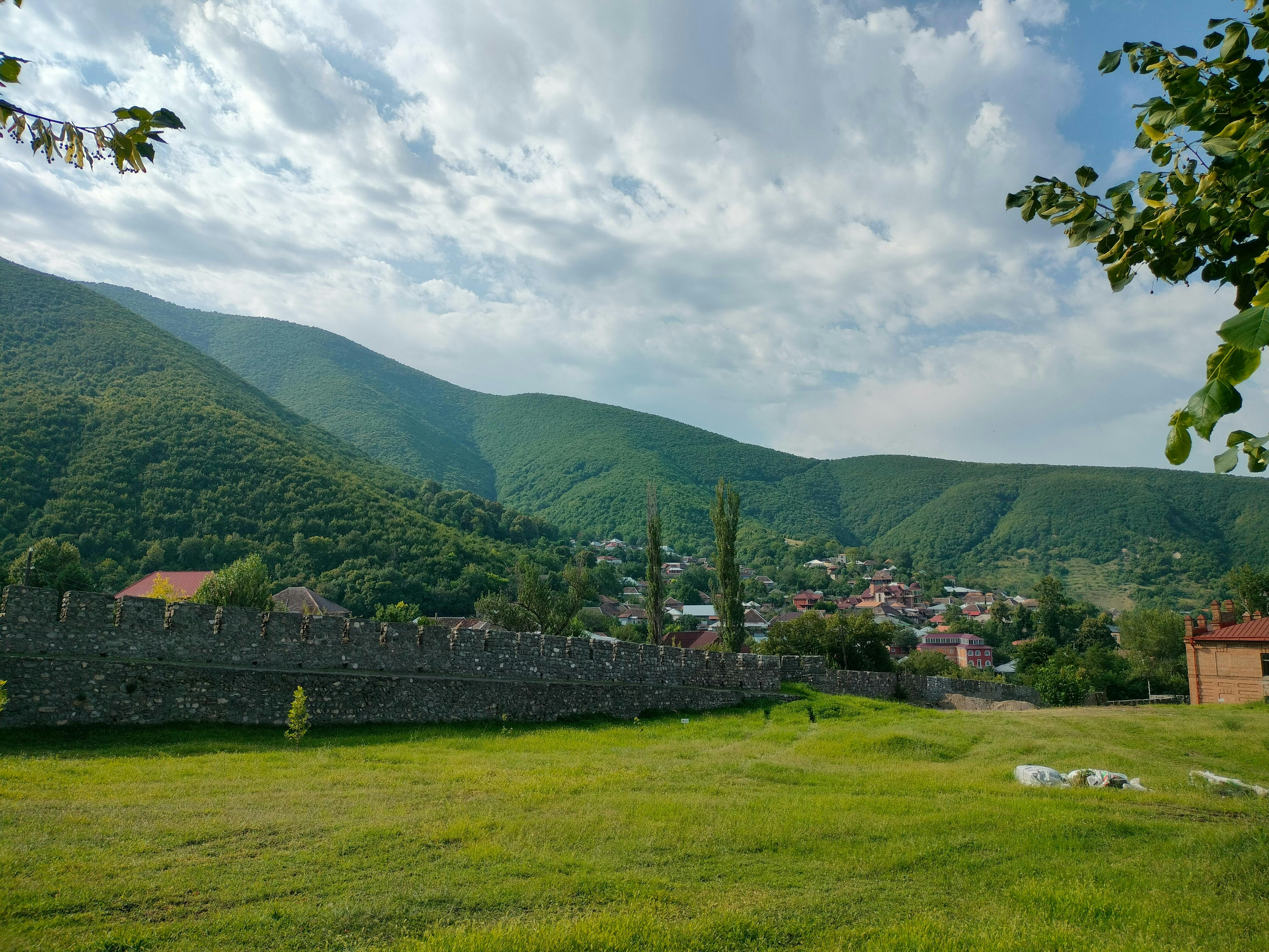 Lush green mountains with a village and stone wall.