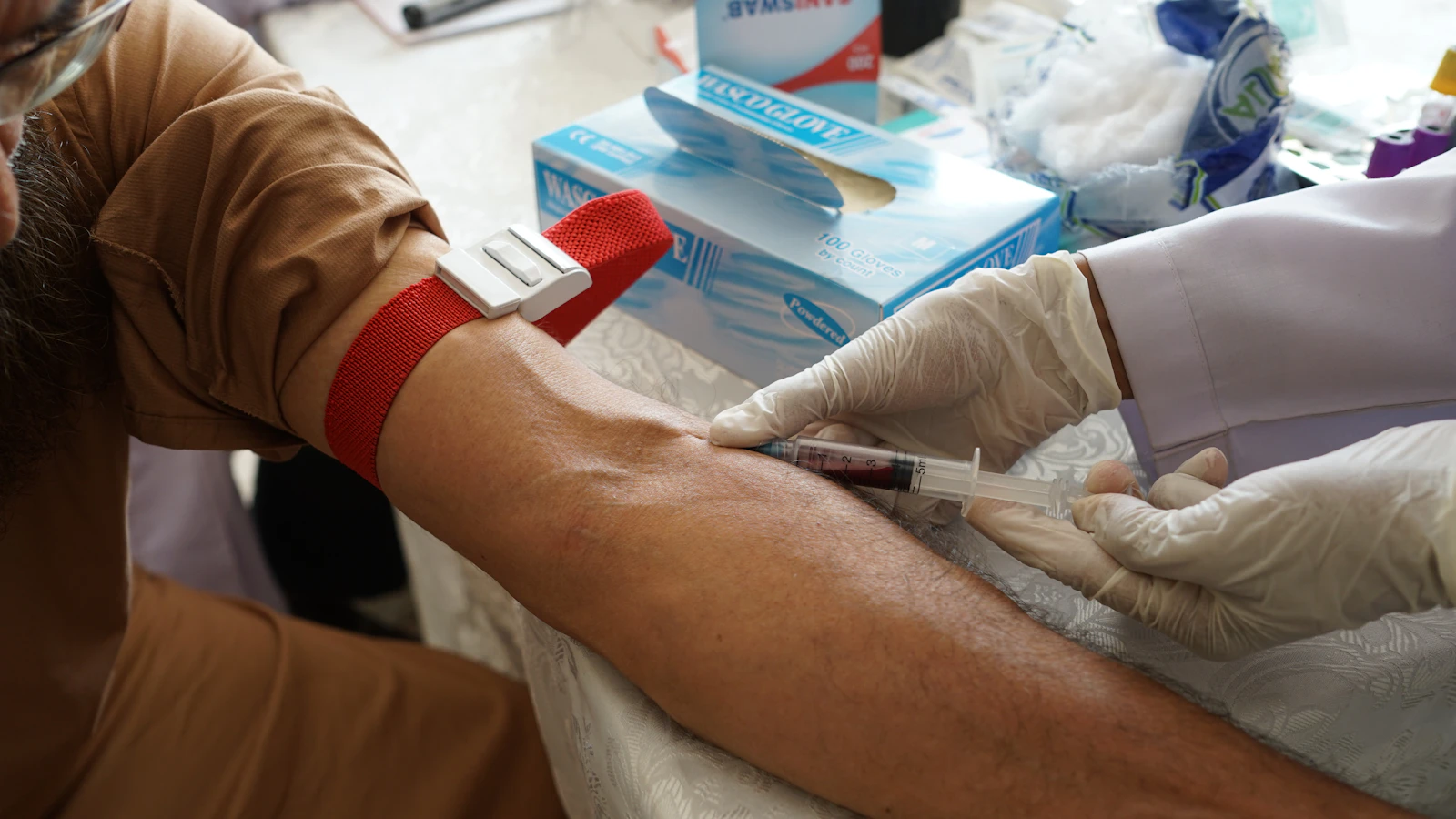 Phlebotomist drawing a blood sample from a patient's arm at home