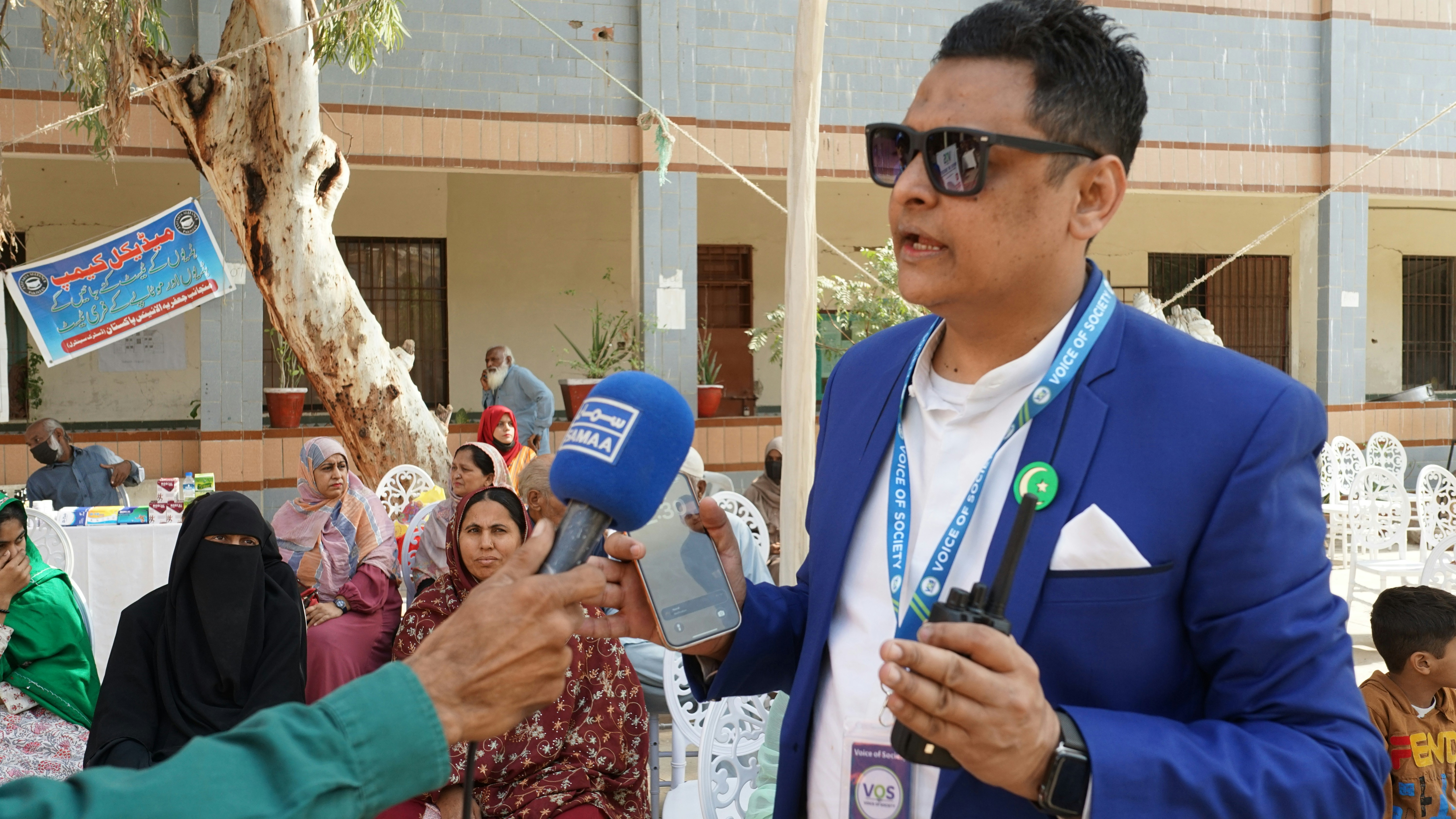 Man in blue suit and sunglasses speaks into microphone