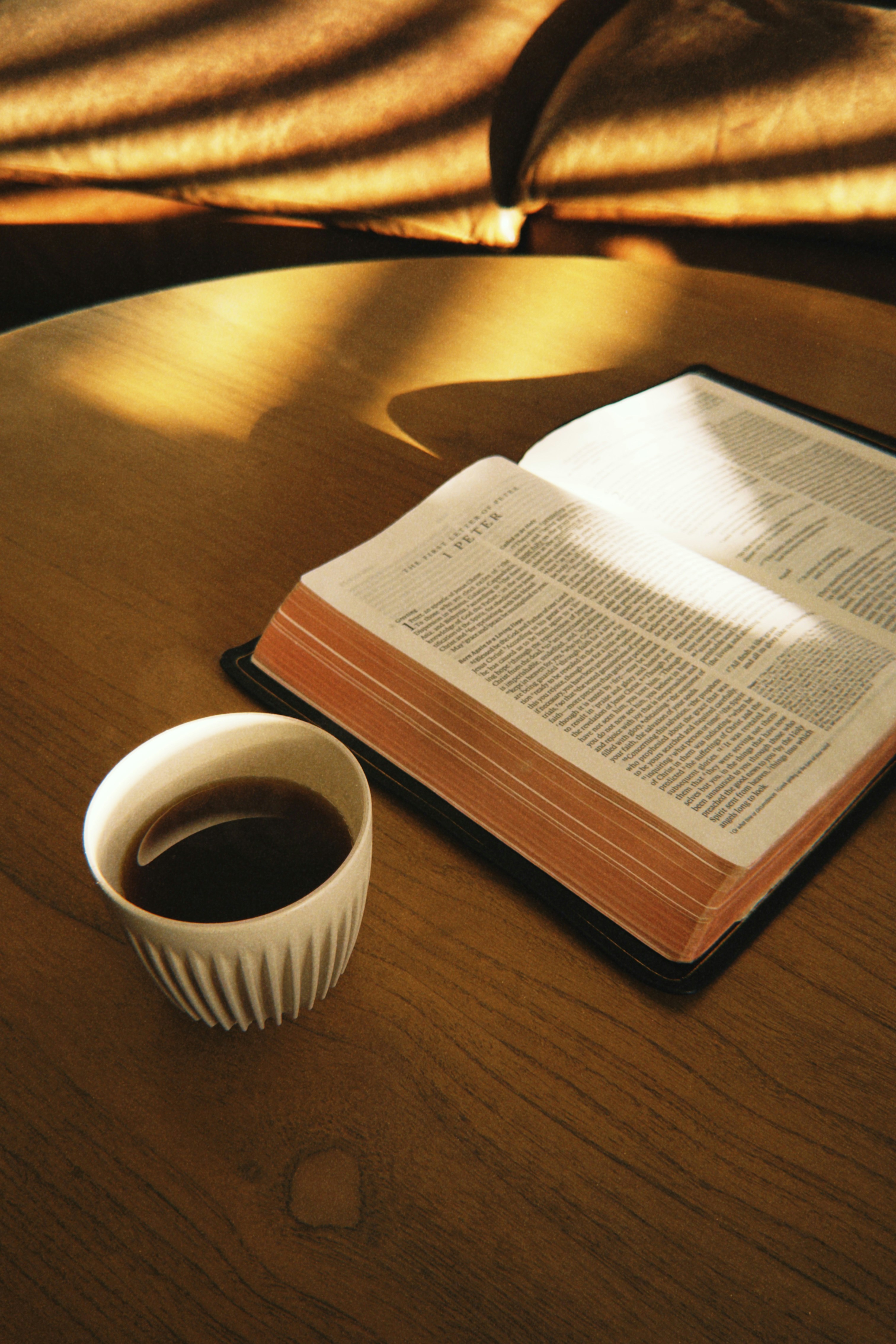 Open bible and coffee cup on a sunlit wooden table