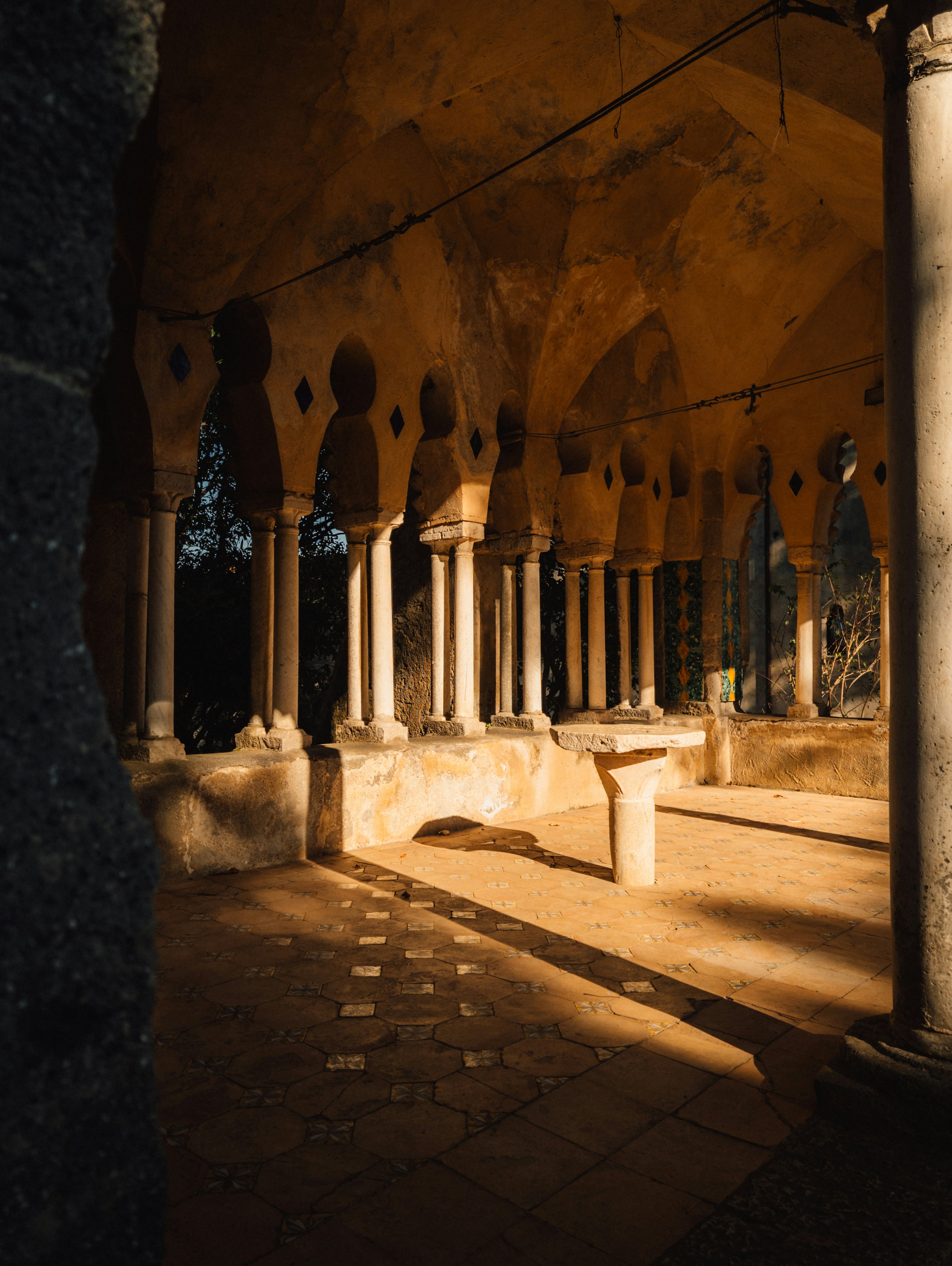Sunlight streams through an ancient arched cloister with columns.