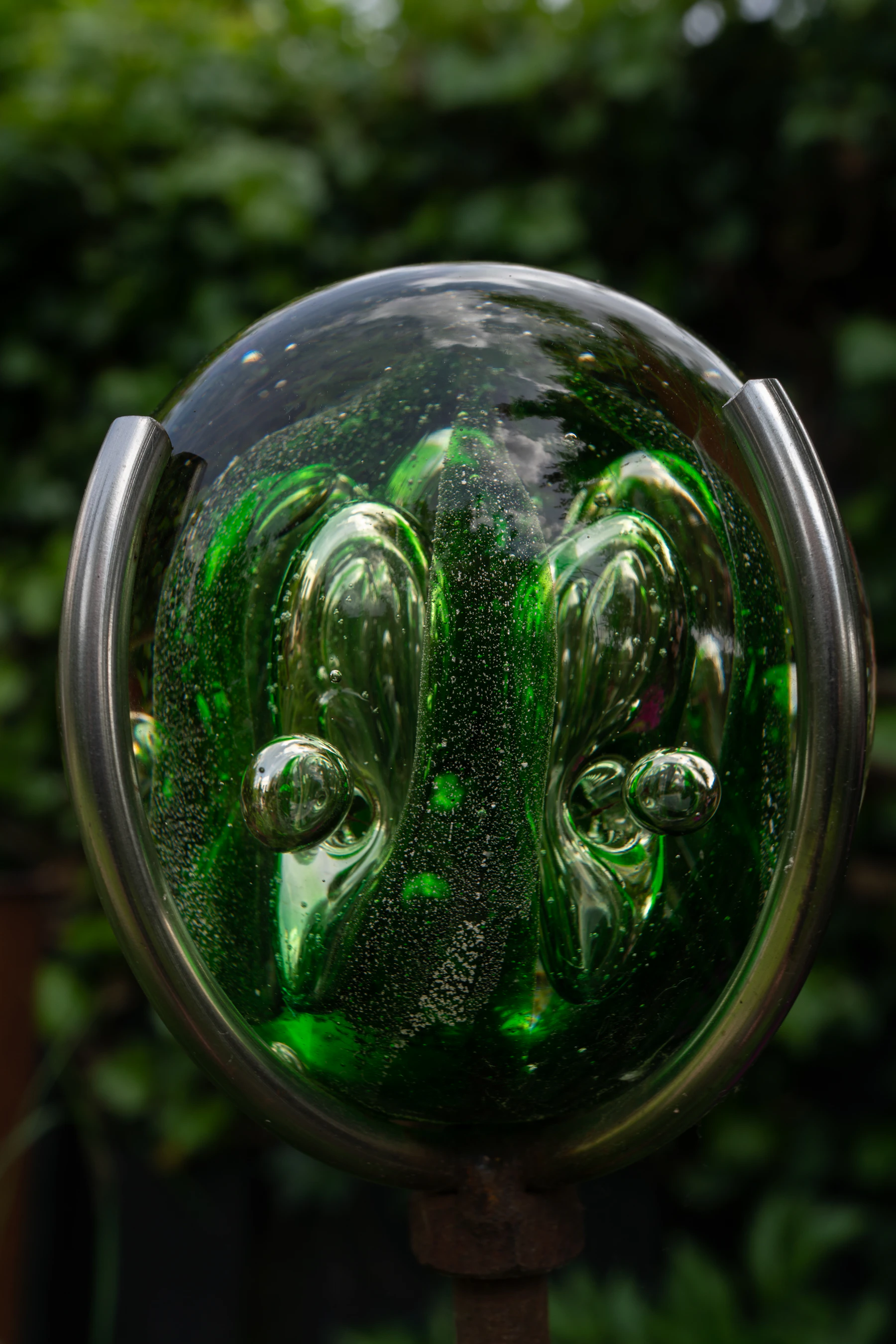 Close-up of a green art-glass orb full of trapped bubbles, held in a steel ring