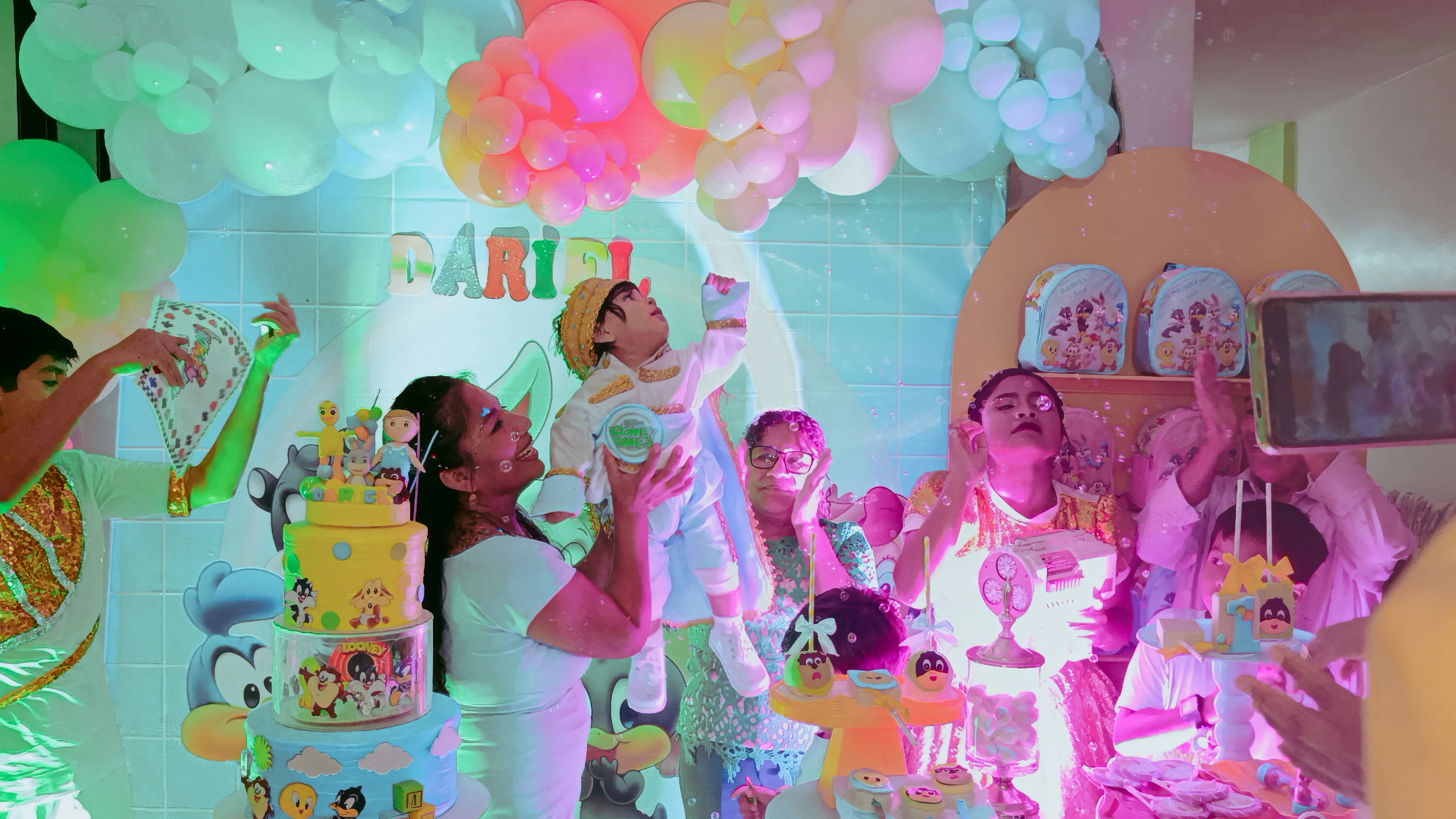 People celebrating baby's birthday with balloons and cakes.