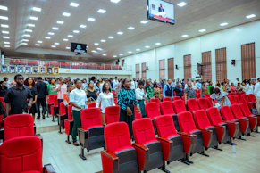 People standing in a large hall with red seats.