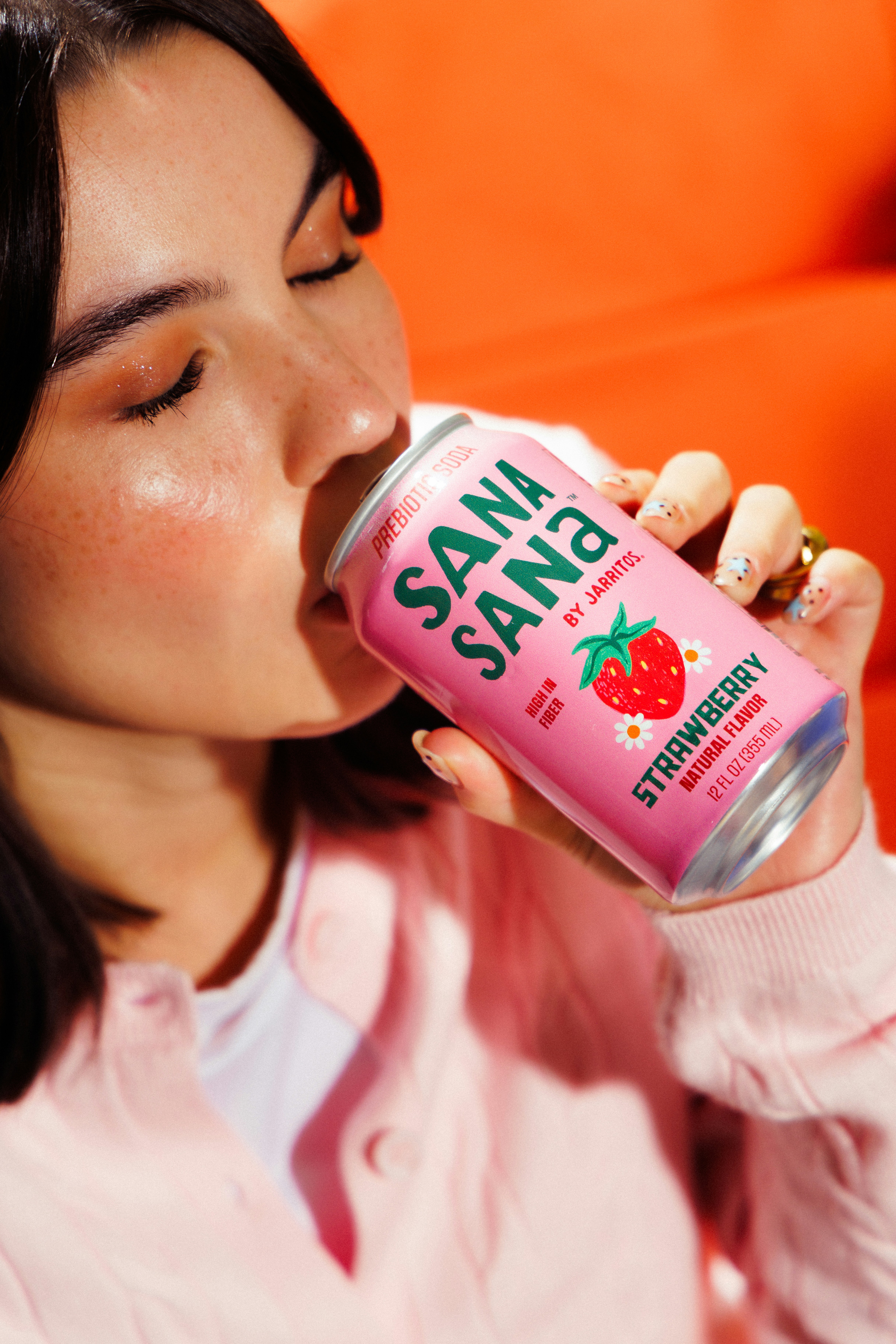 A young woman drinks from a pink strawberry-flavored can