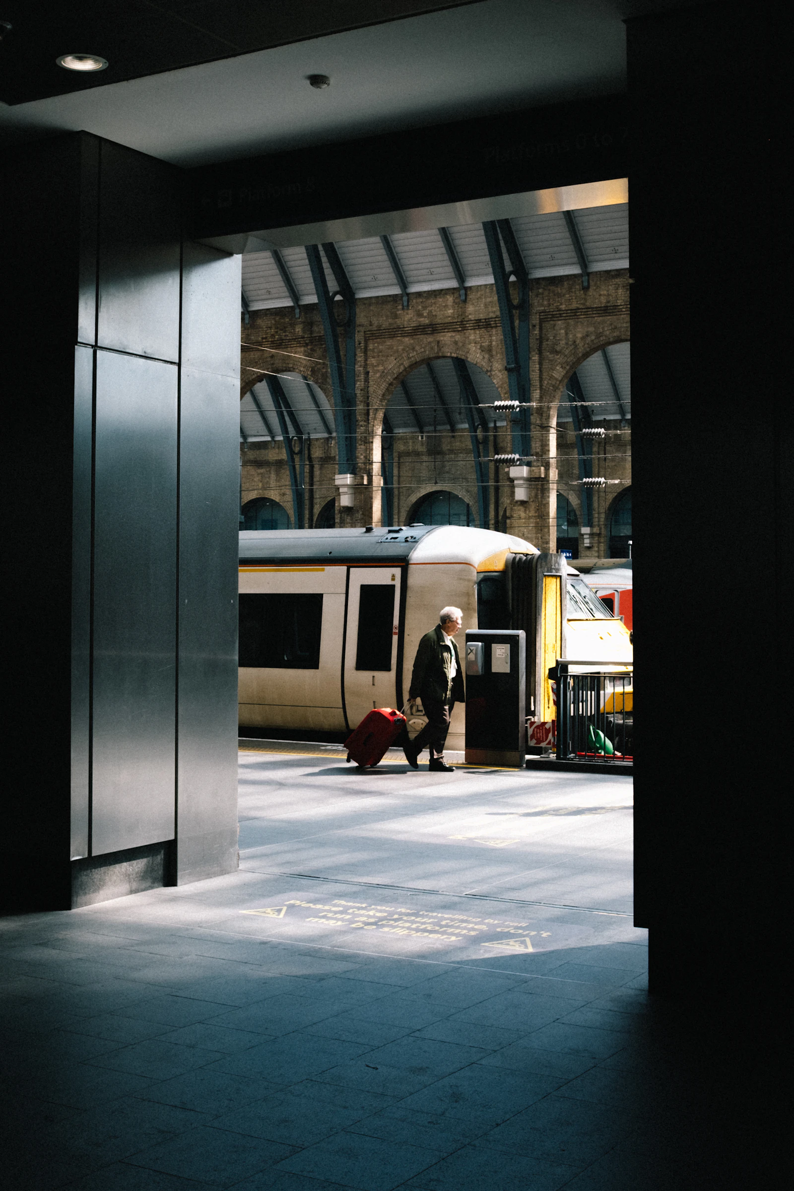 A traveller rolling a red suitcase along a railway platform.