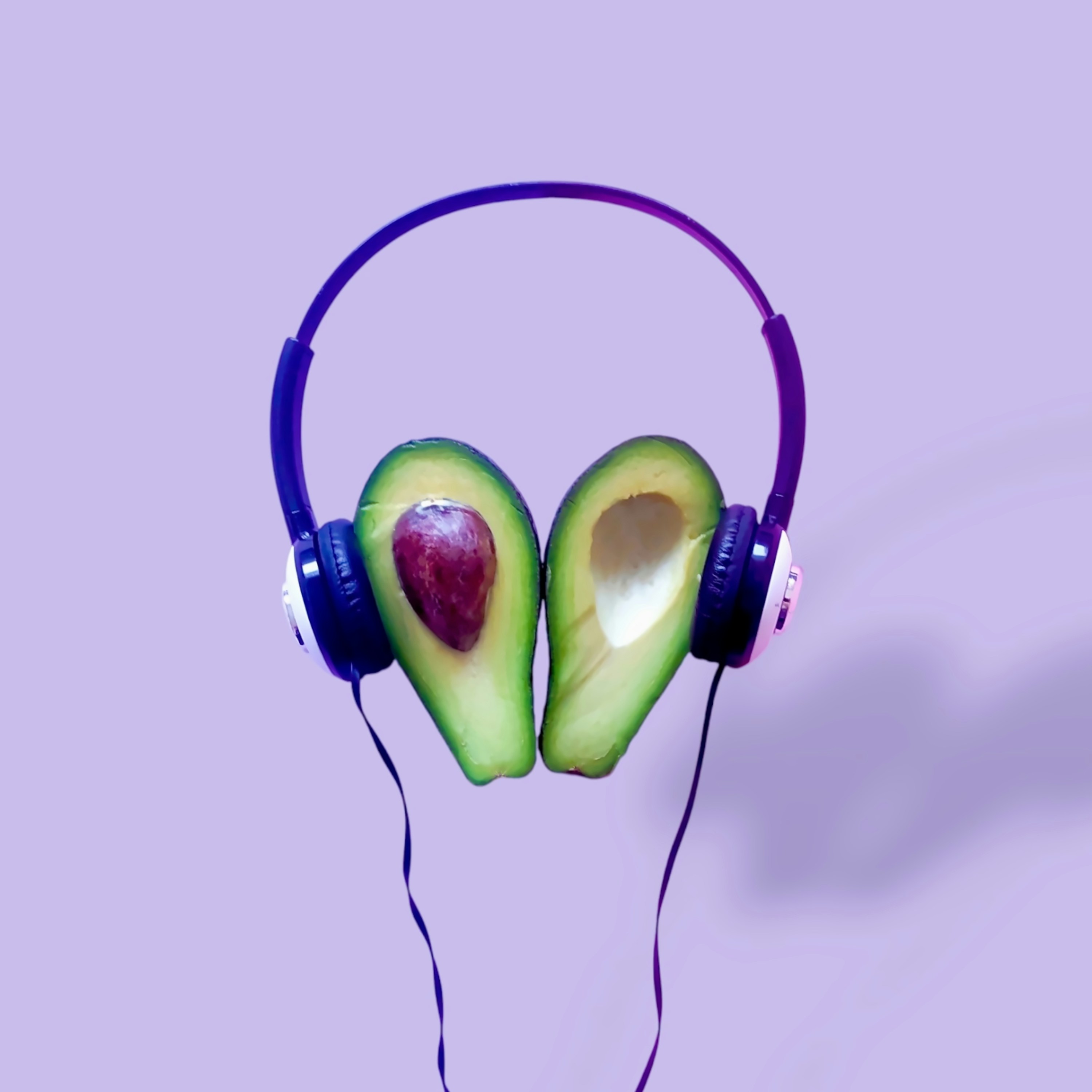 Two avocado halves wearing headphones on purple background
