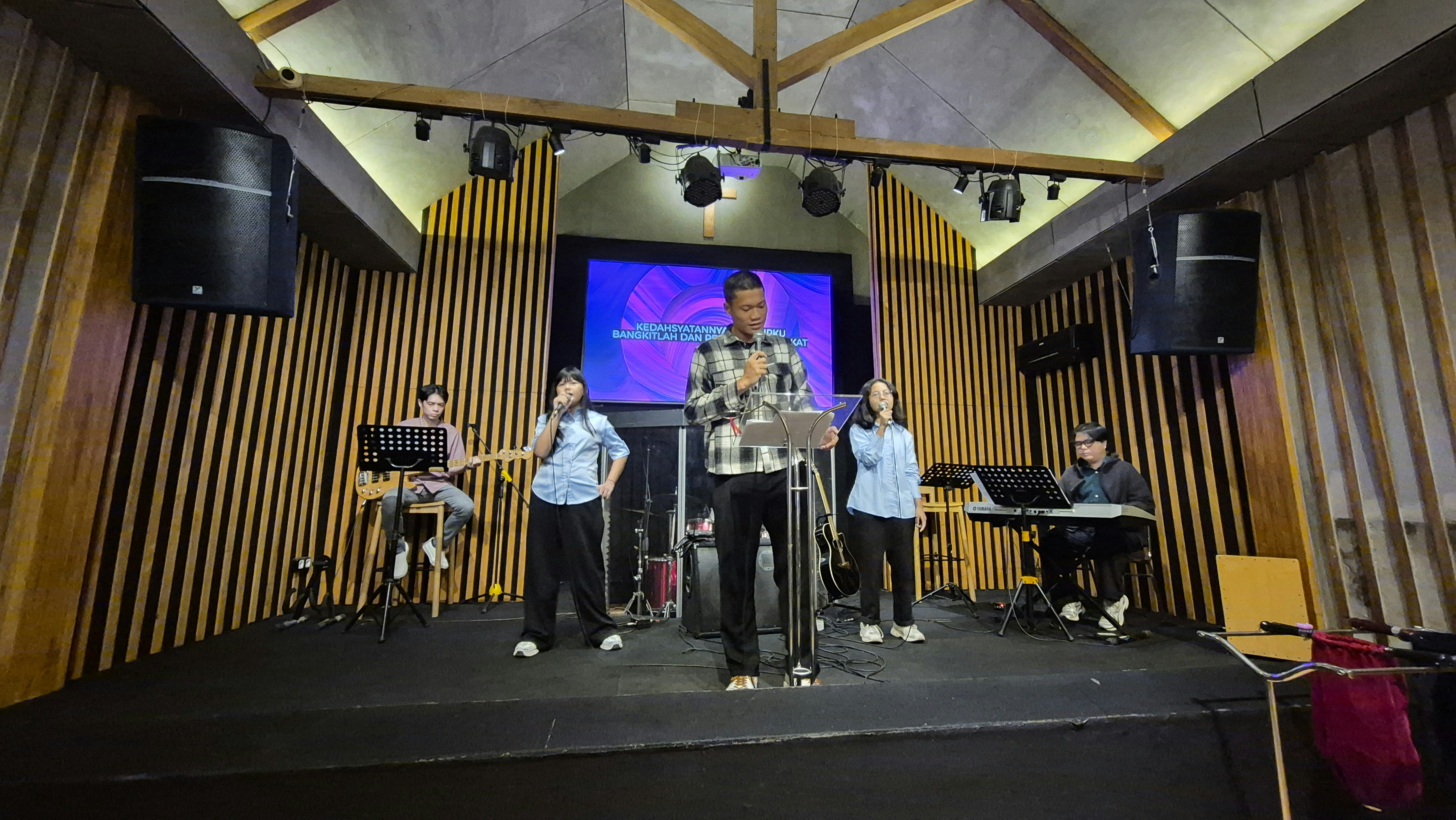Un grupo actúa en un escenario con una pantalla grande.