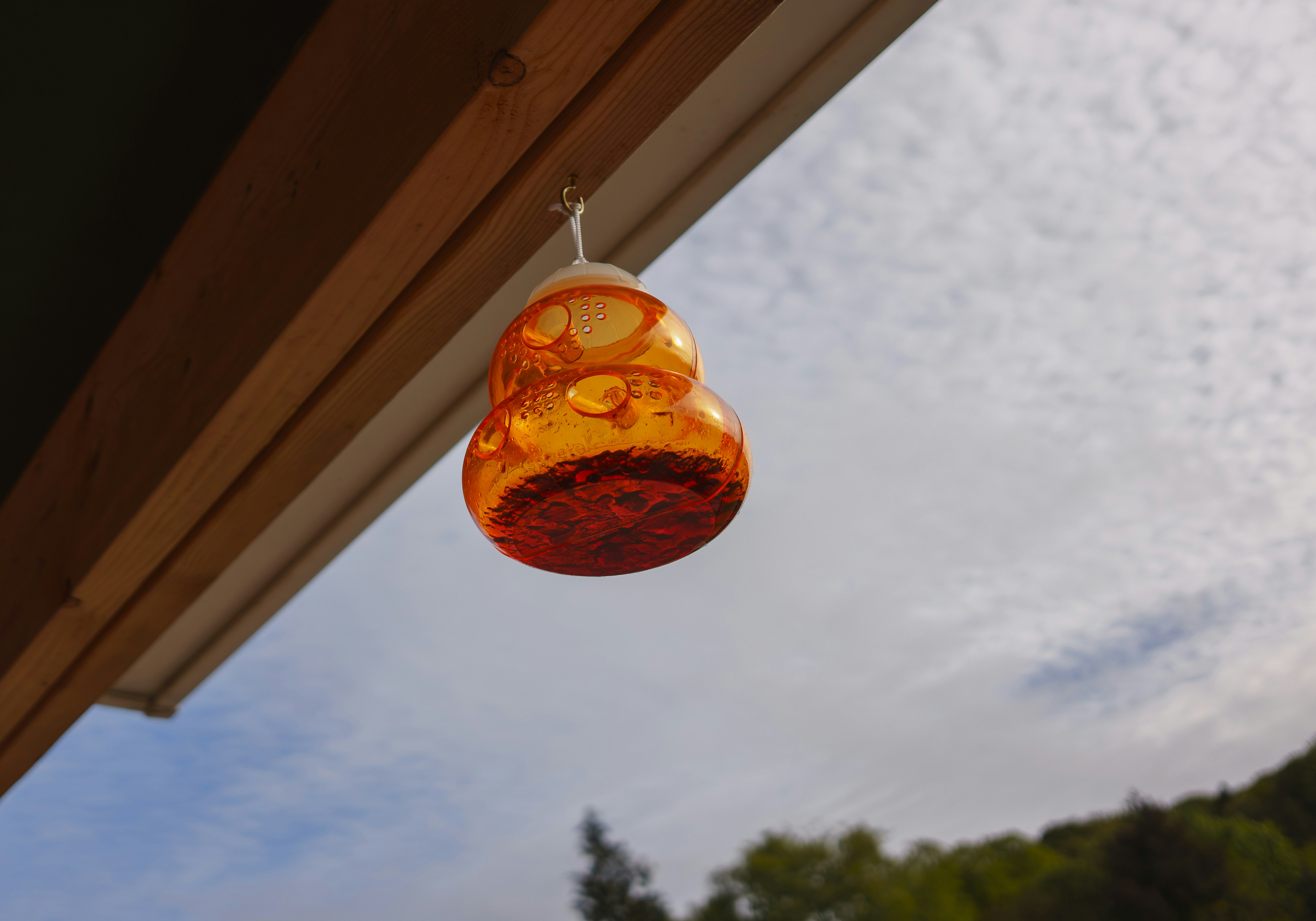 Gourd-shaped orange glass hangs from eave under cloudy sky.