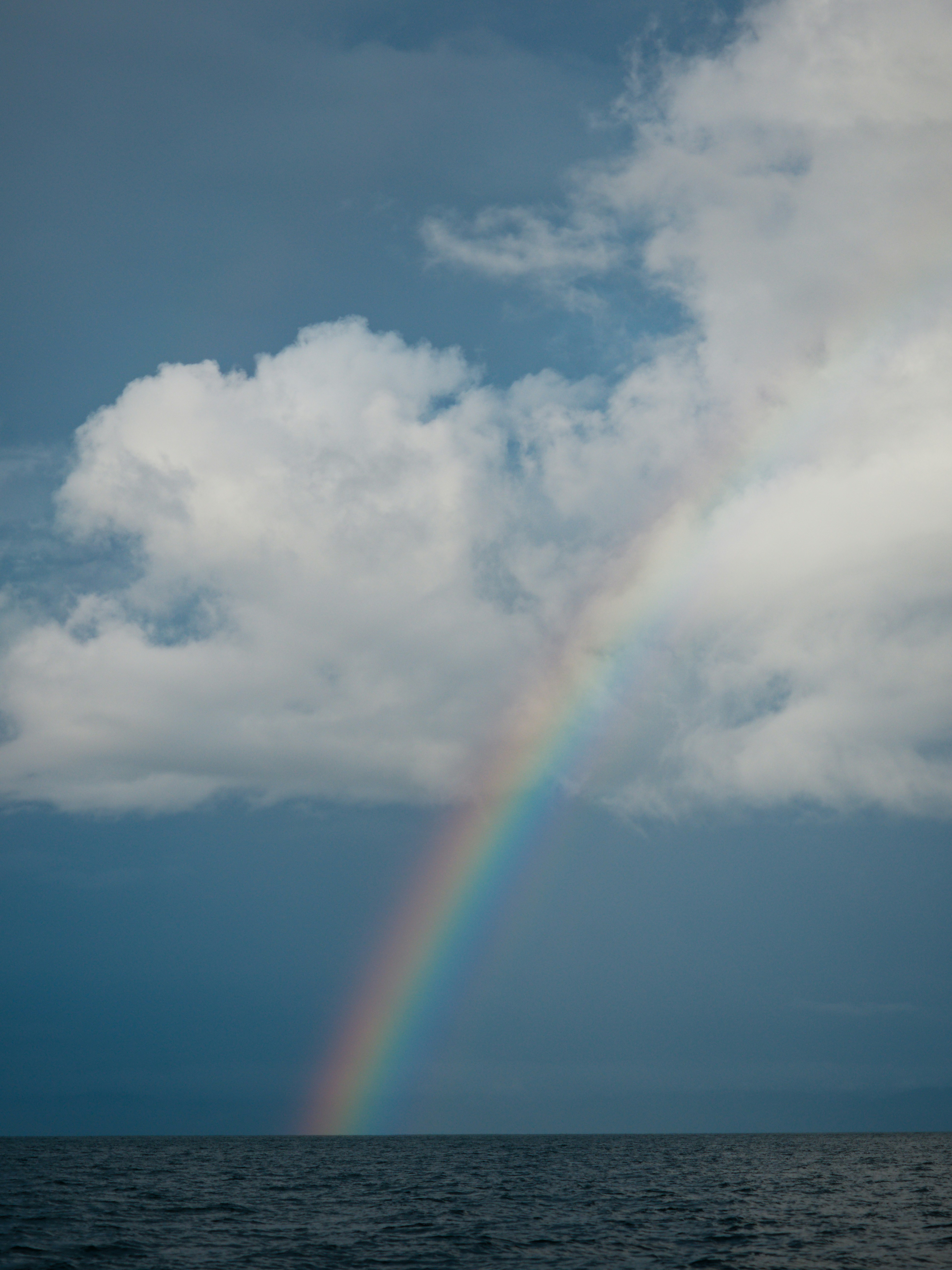 A rainbow arches over the dark ocean under clouds