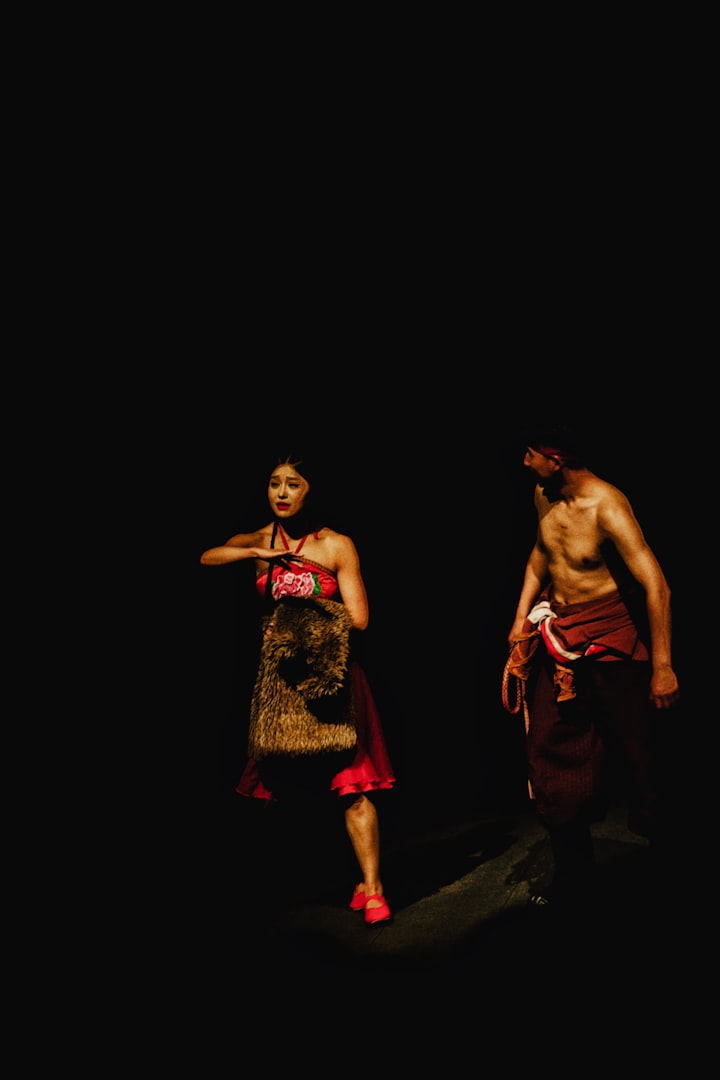 Two performers on a darkened stage, mid-scene, anonymized in low key light