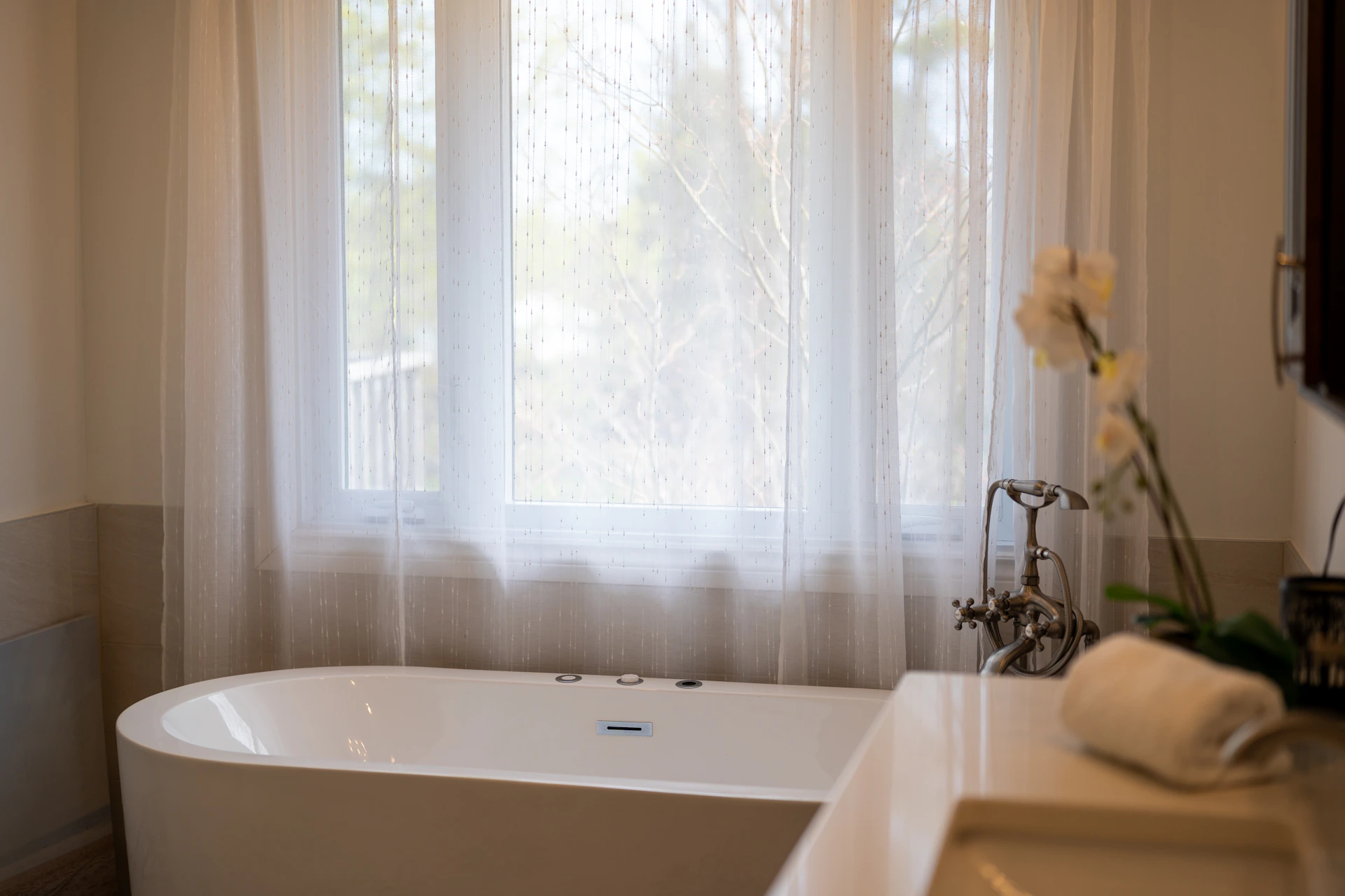 A modern bathtub with sheer curtains and a sink