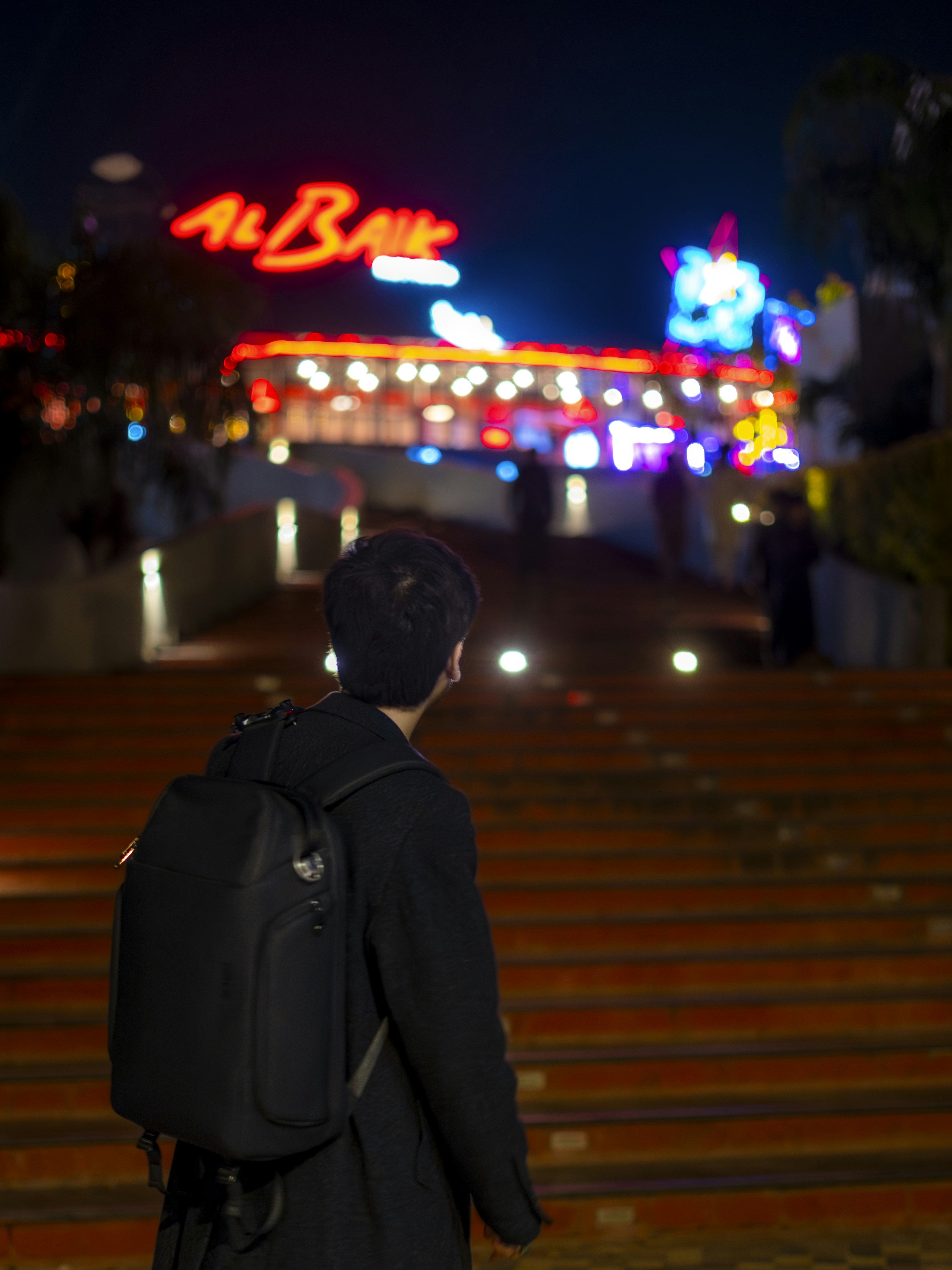 リュックを背負った人が夜に明るく照らされた建物を見渡す。