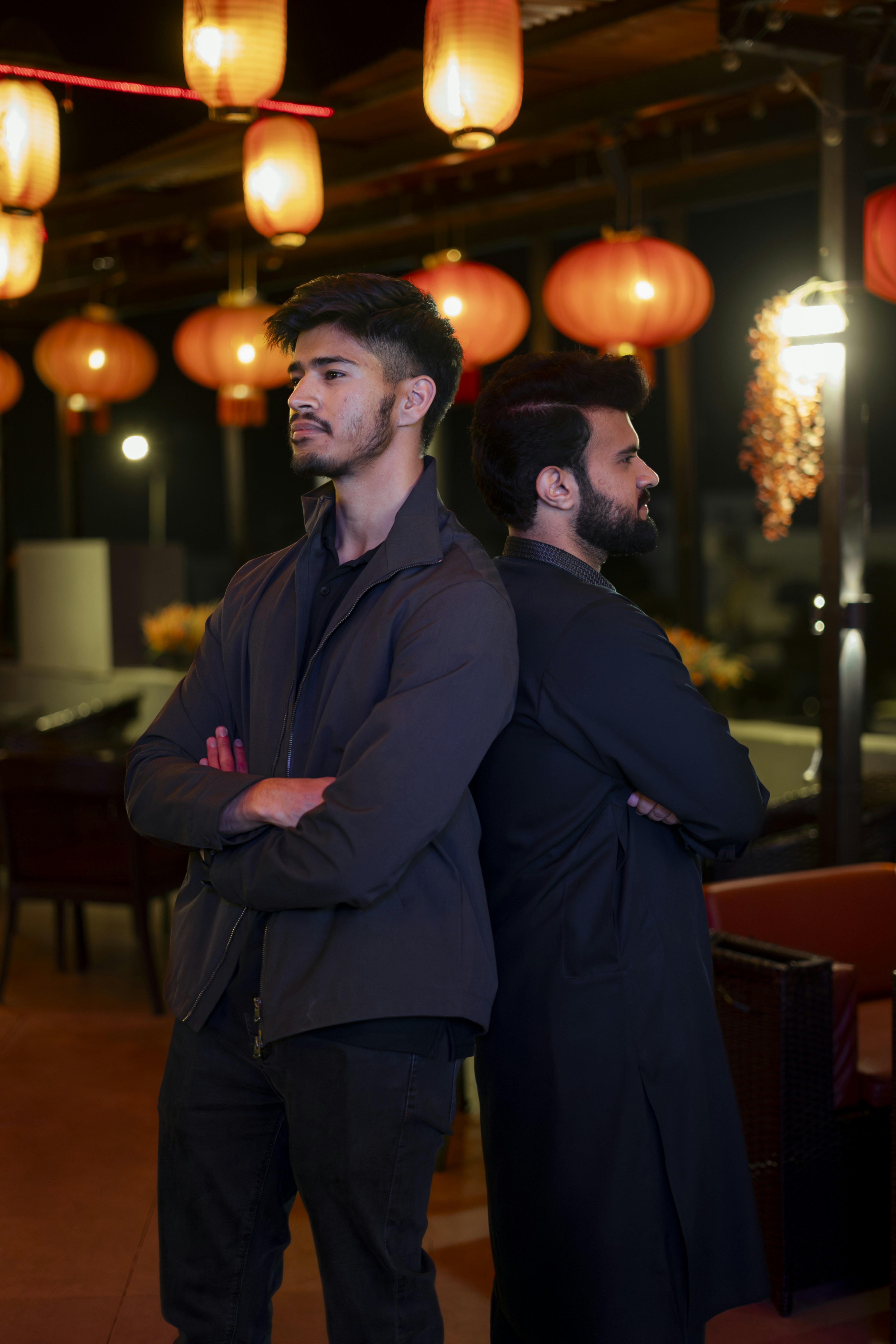 背中合わせに並び、腕を組み、赤いランタンを掲げた二人の男。