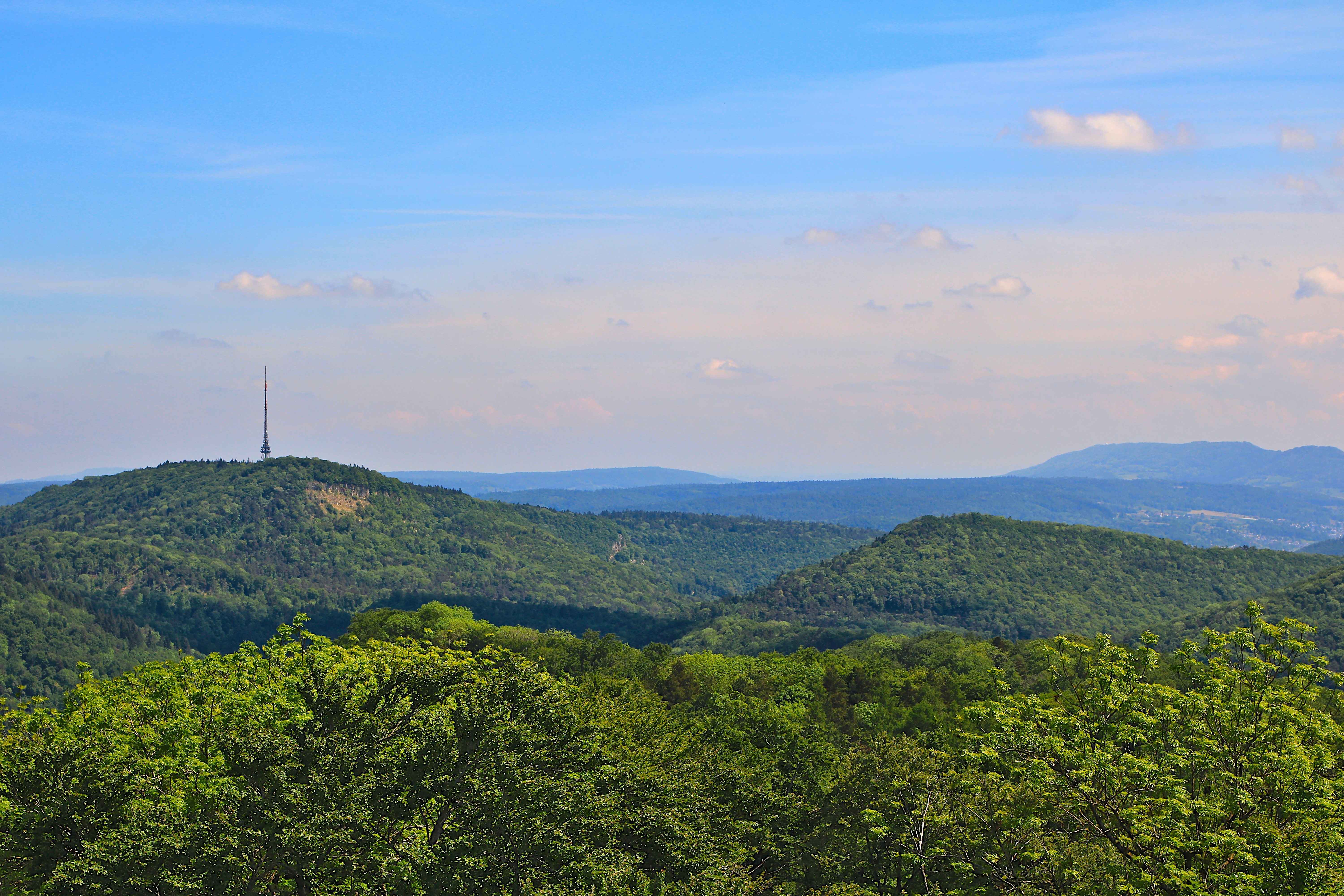 Paesaggio montuoso verde con una torre di comunicazione distante.