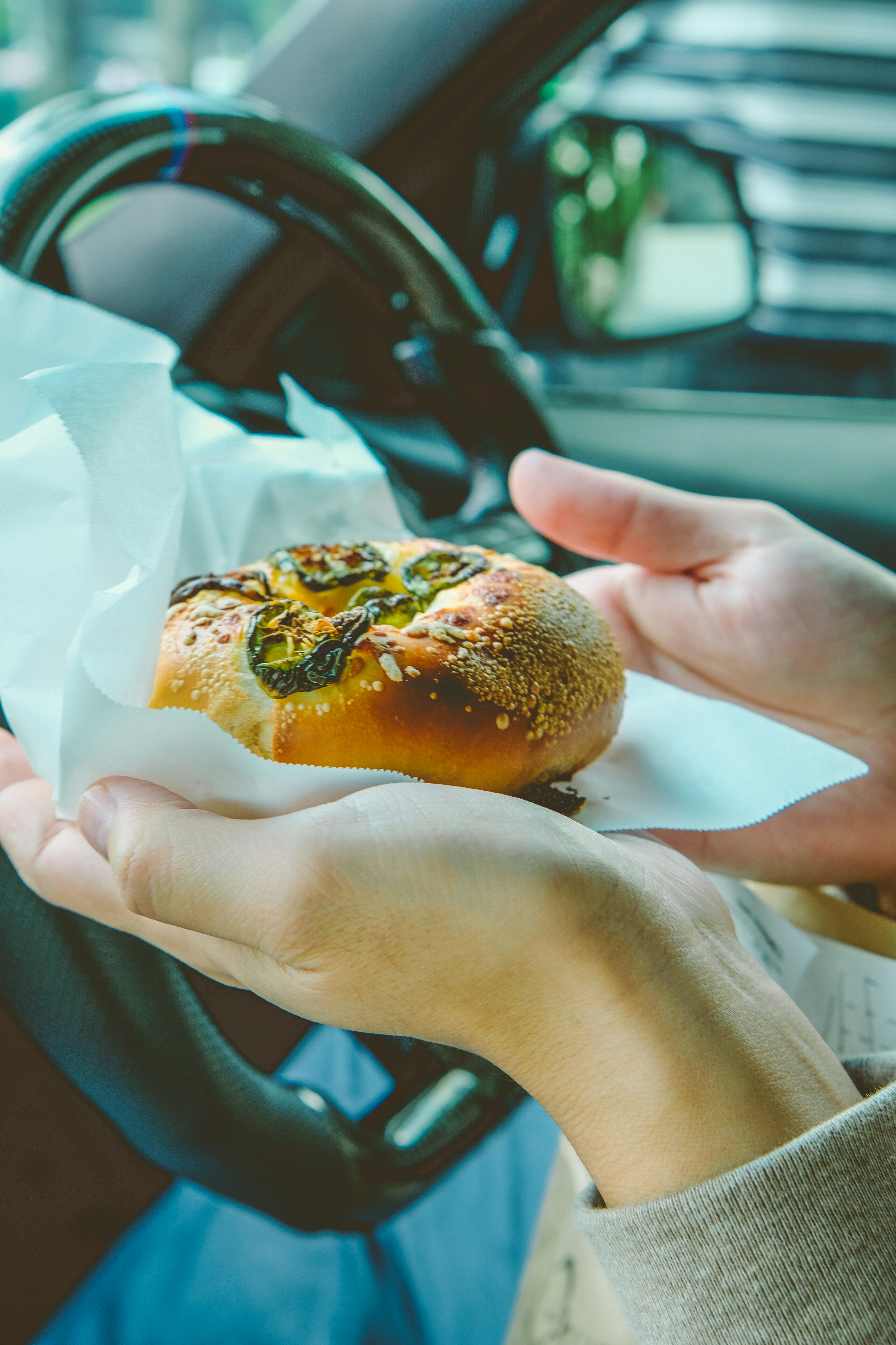 Tangan memegang roti jalapeno keju di dalam mobil.