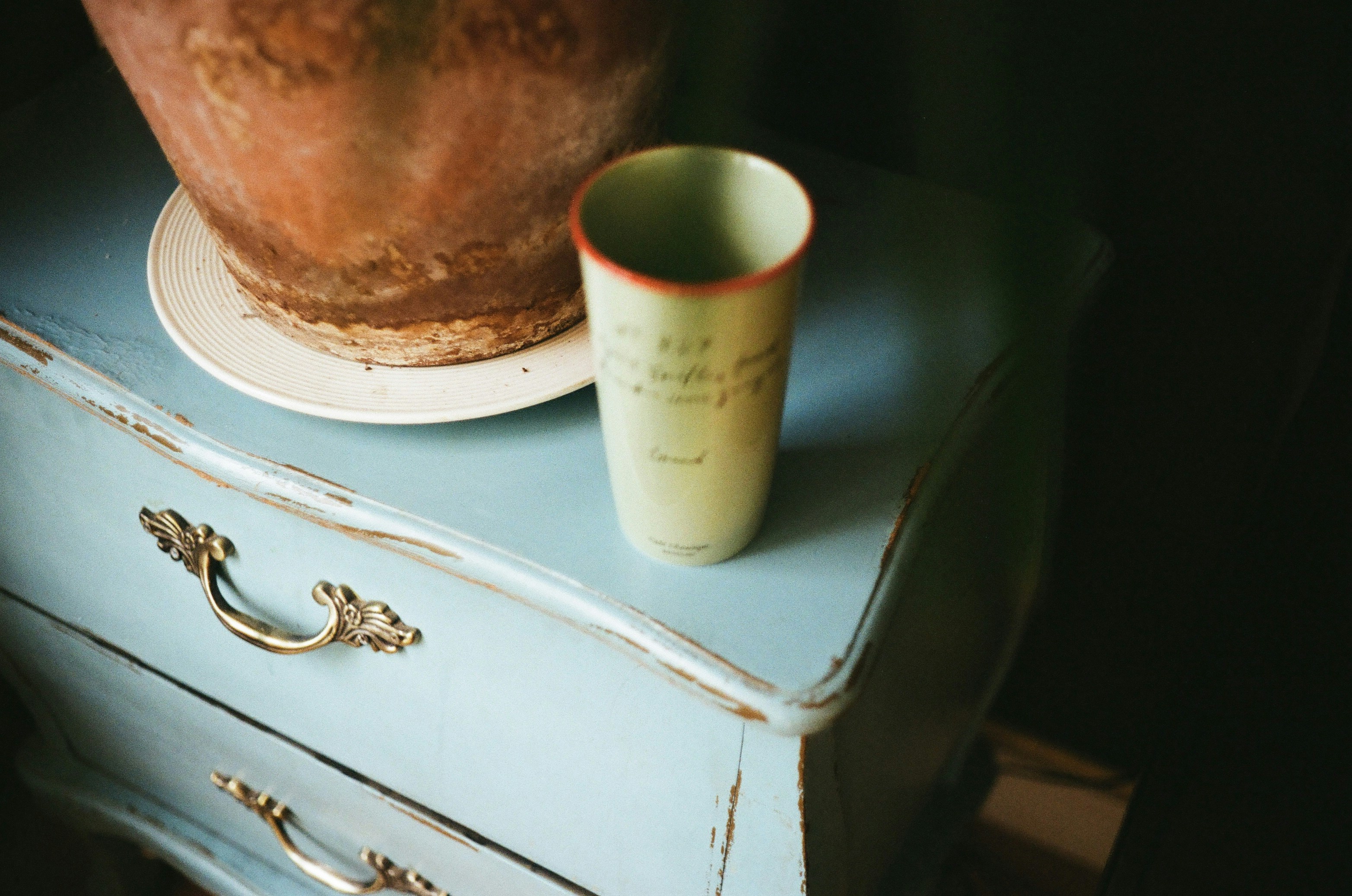 A pale green cup sits on a blue dresser.