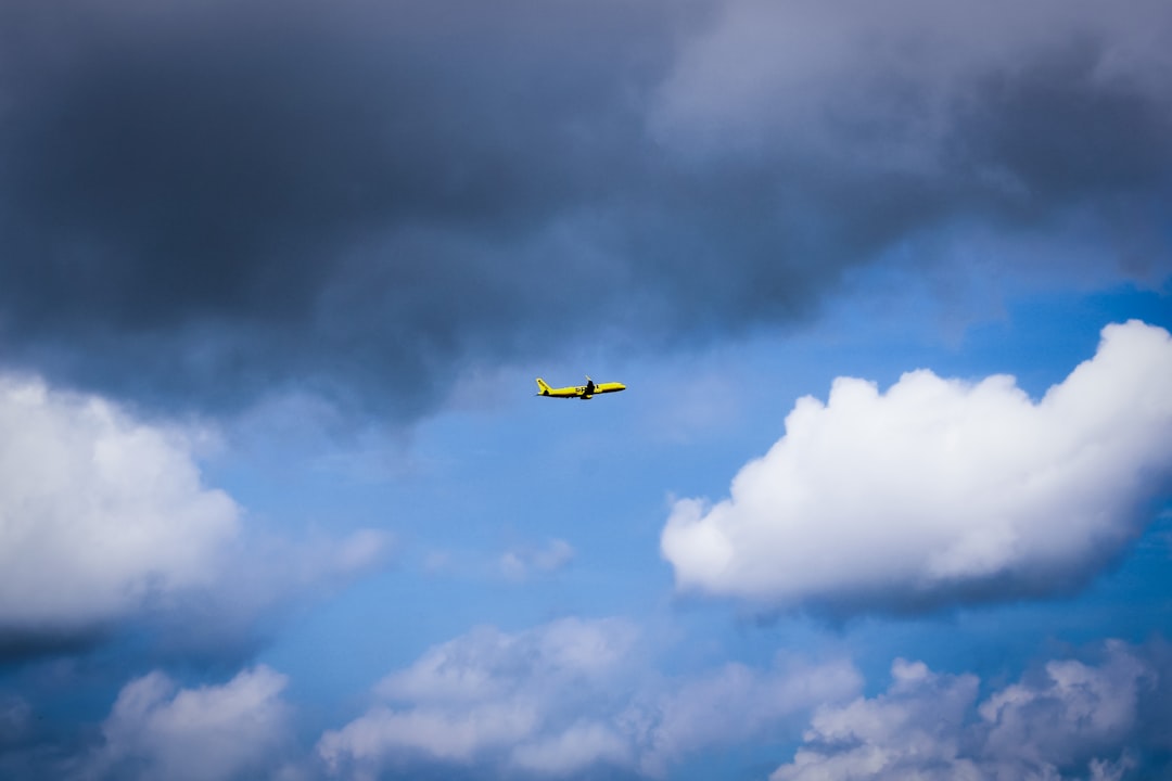 A small yellow airplane flies through a cloudy blue sky.