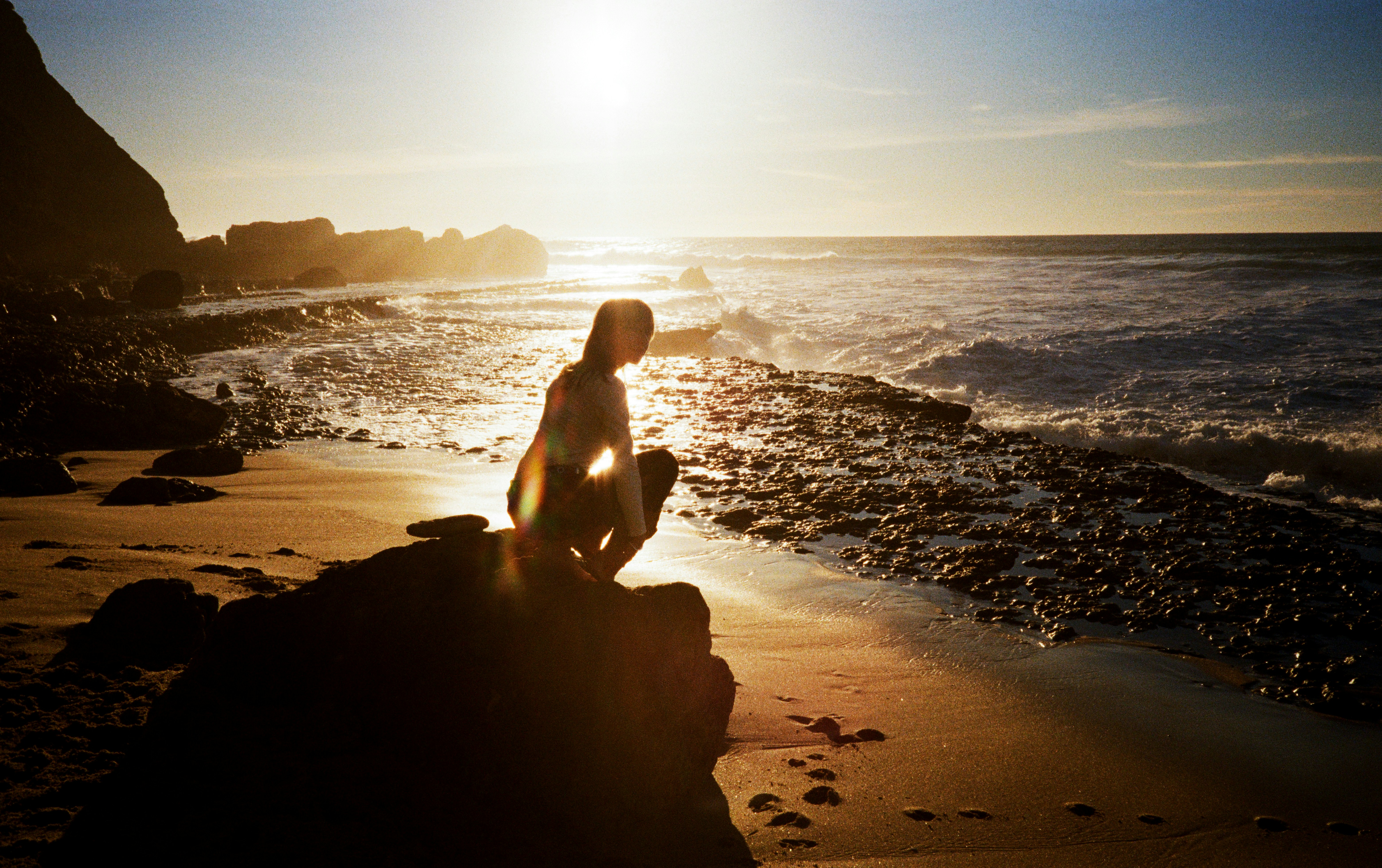 Photo of Woman crouching on a rocky beach at sunset by Tanya Prodaan