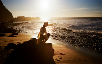 Woman crouching on a rocky beach at sunset