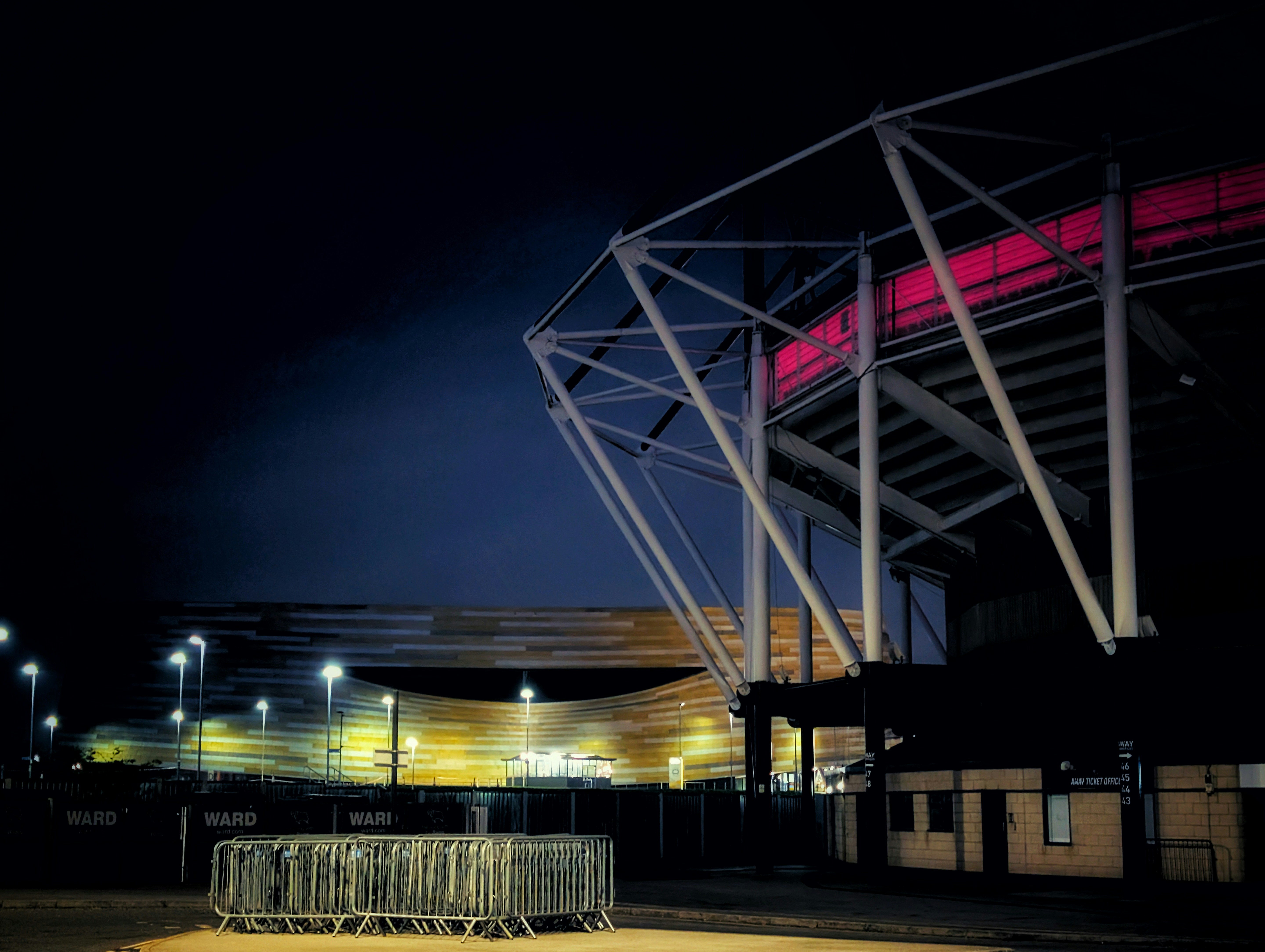 Uno stadio di notte con luci intense e barriere metalliche.