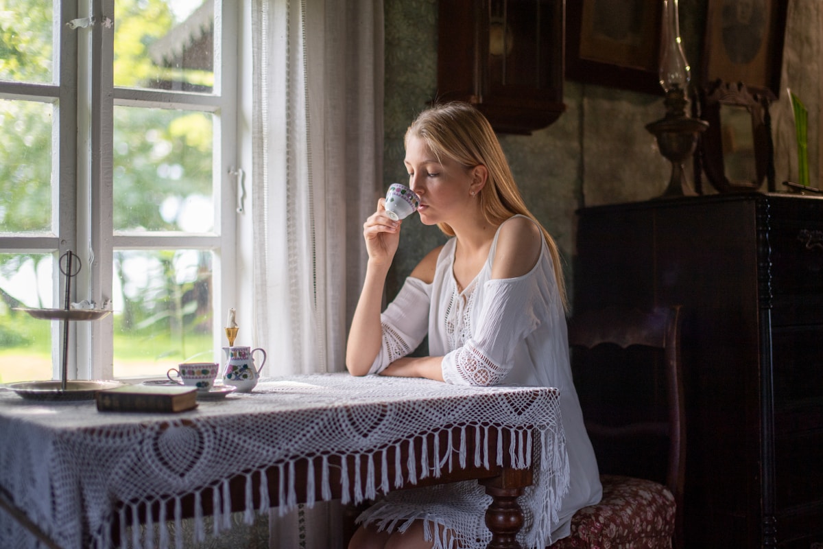 A young woman sips tea by a window.