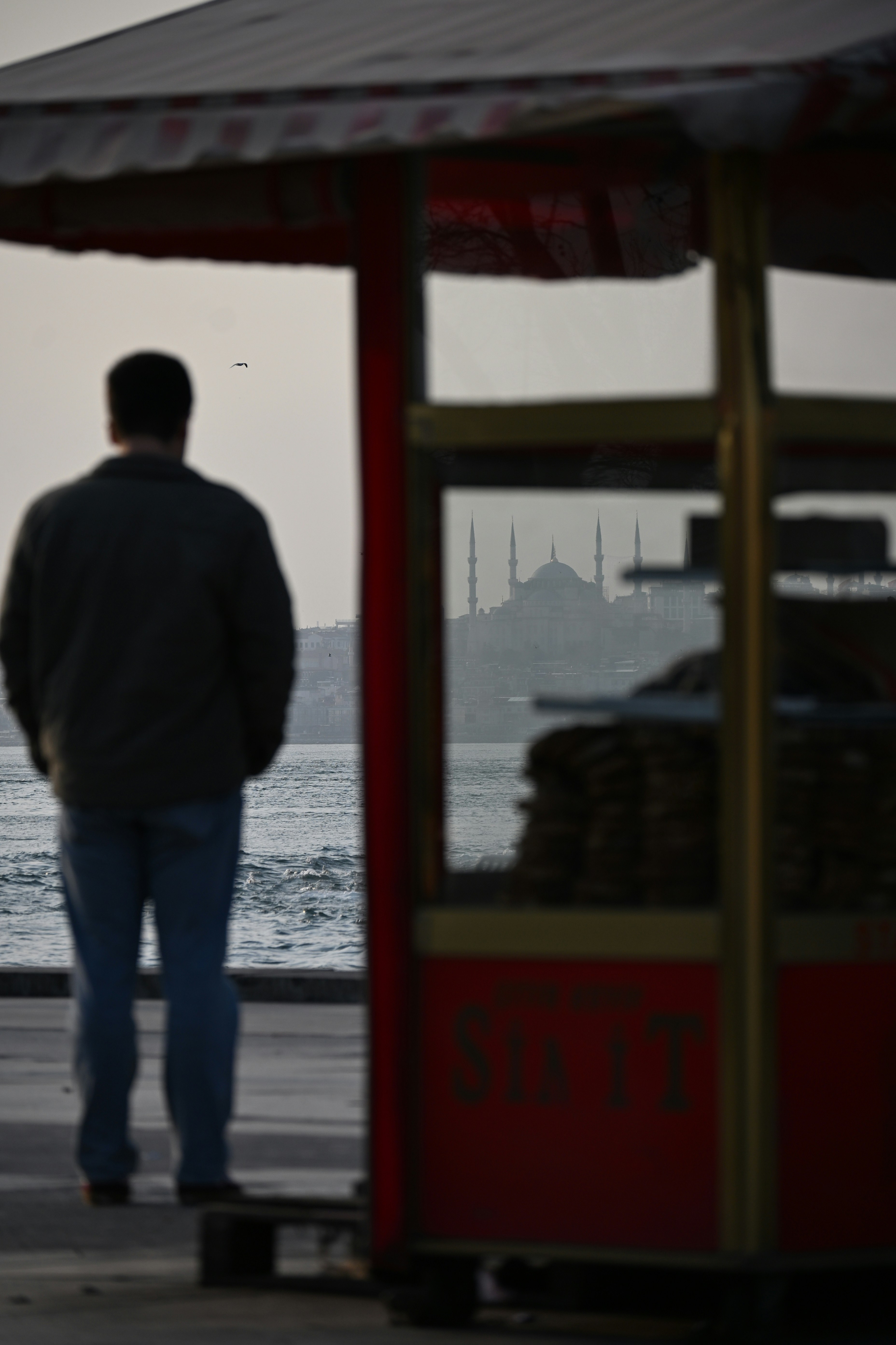 Un homme se tient près de l’eau, regardant la silhouette lointaine de la mosquée.