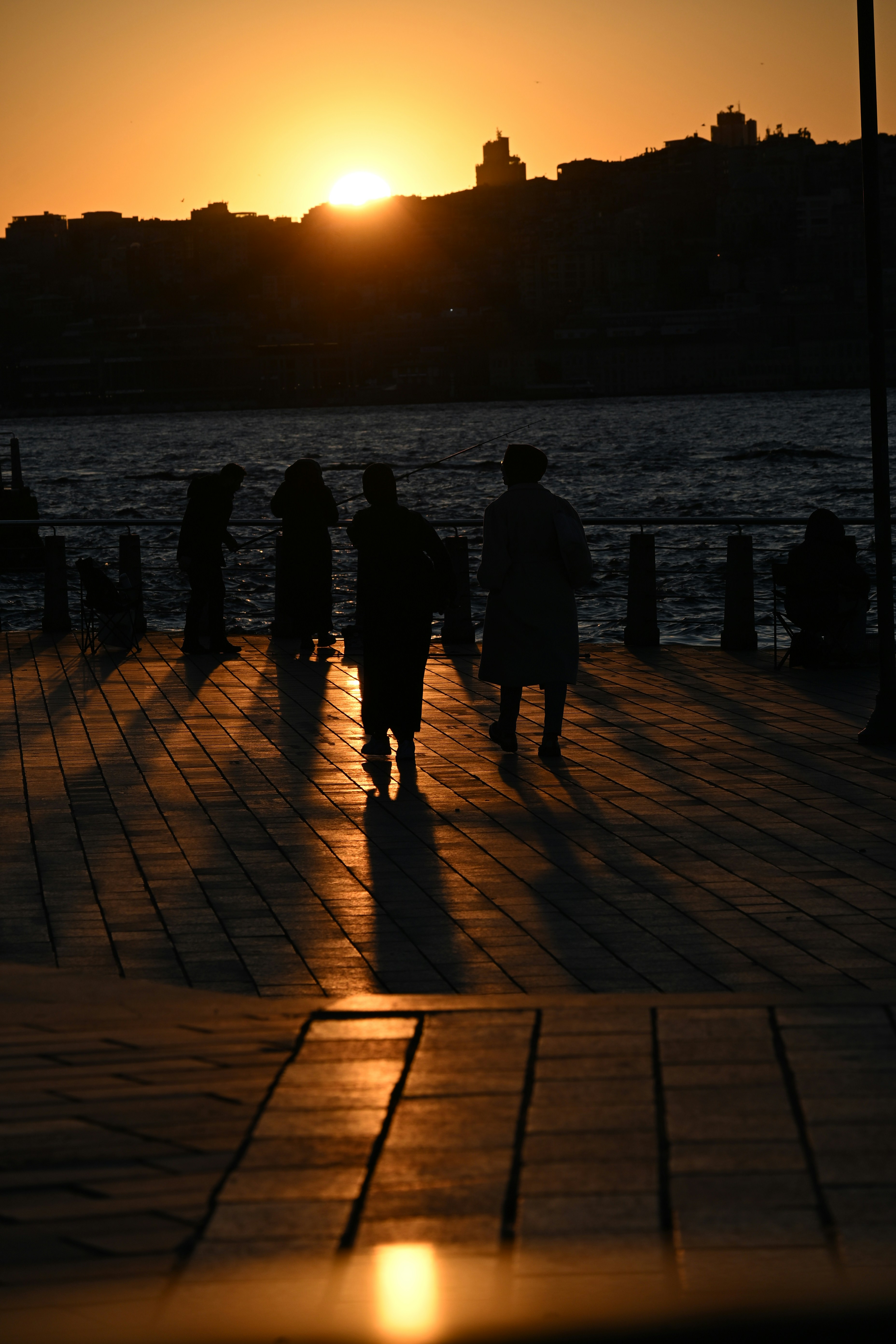 Des silhouettes de personnes marchant sur une jetée au coucher du soleil.