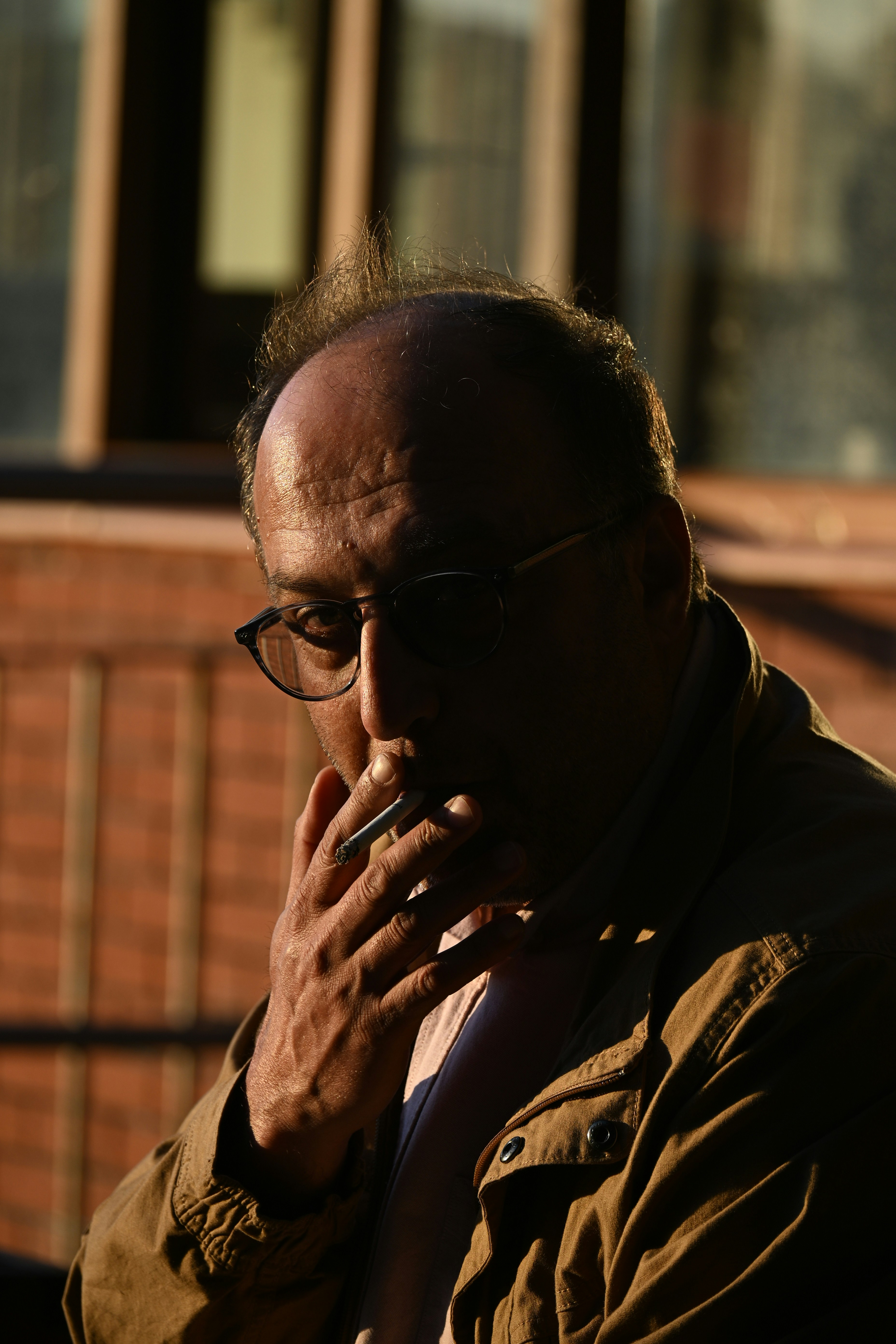 Un homme à lunettes fumant une cigarette au soleil.