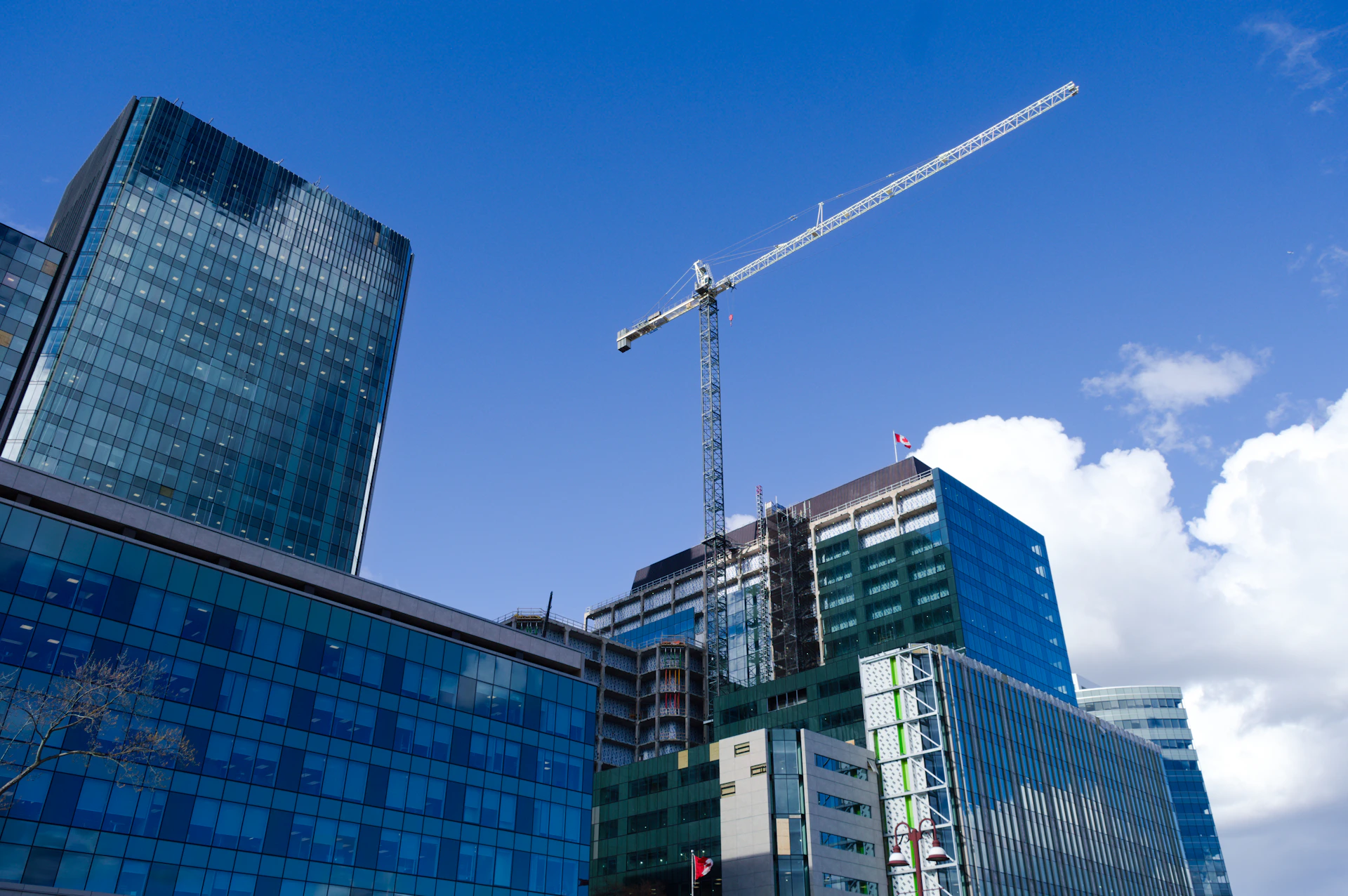 Modern glass buildings and construction crane under blue sky.