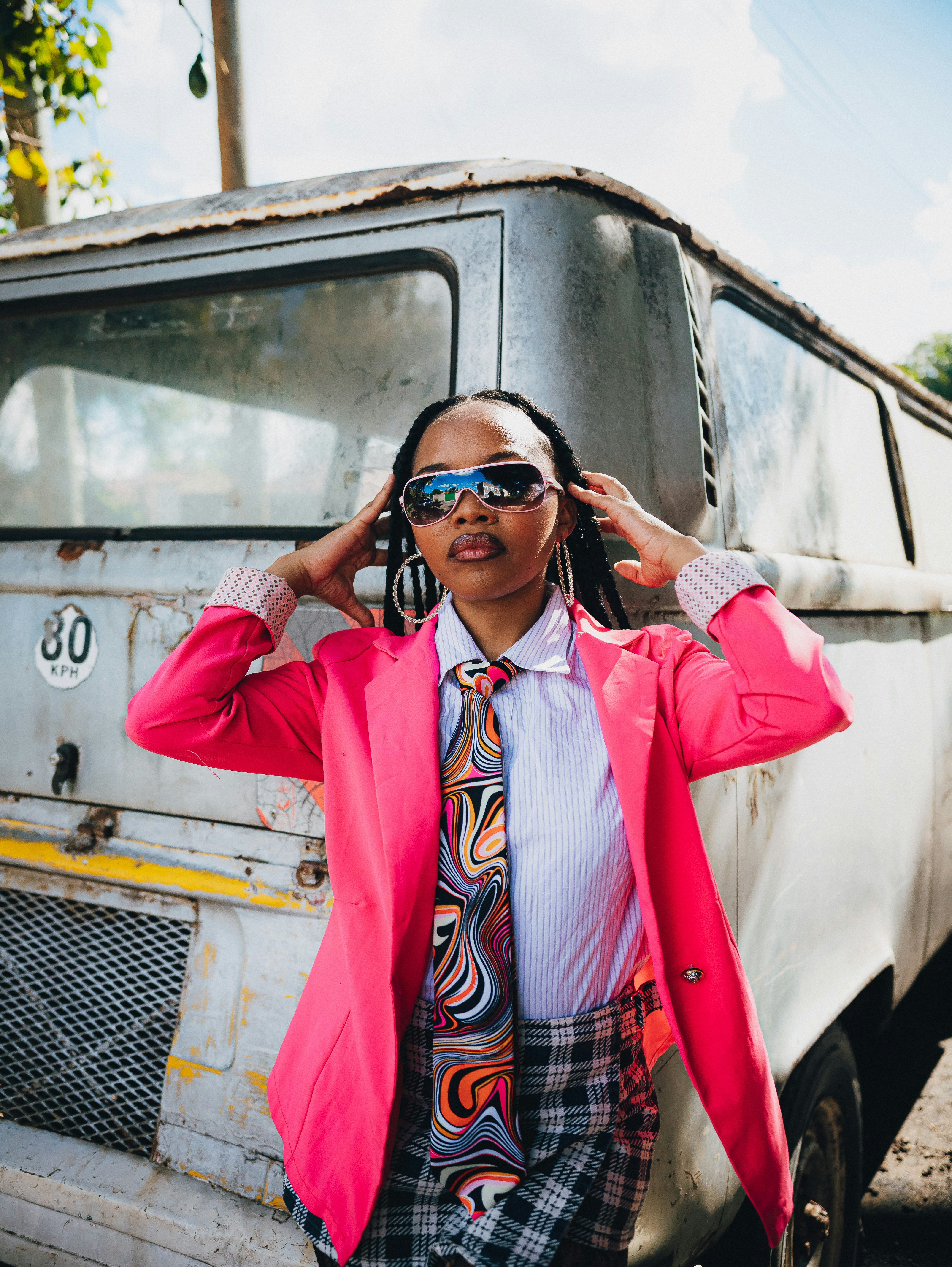 Mulher de blazer rosa e óculos escuros perto de uma van velha