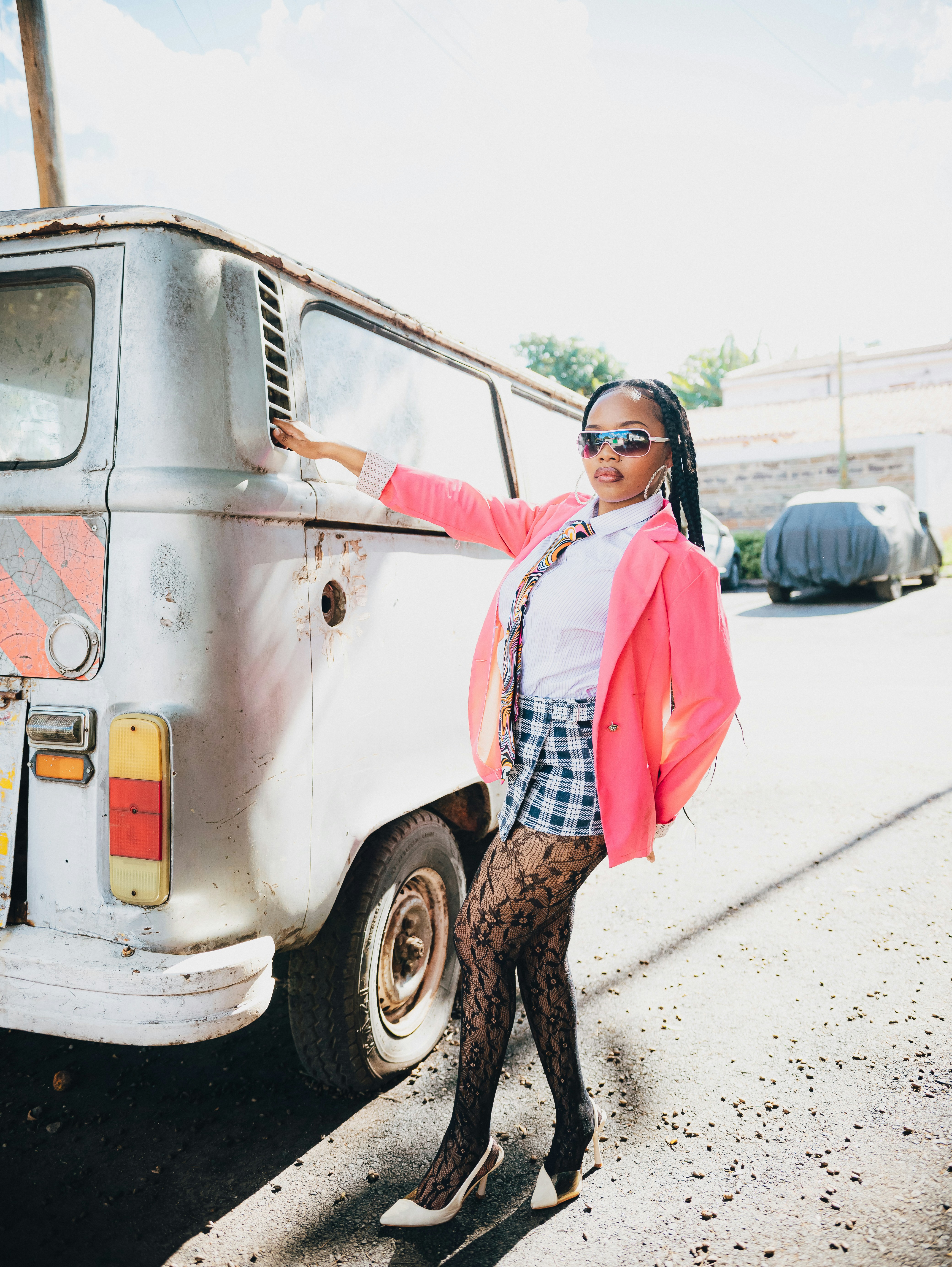 Mulher estilosa com blazer rosa posa ao lado de uma van vintage