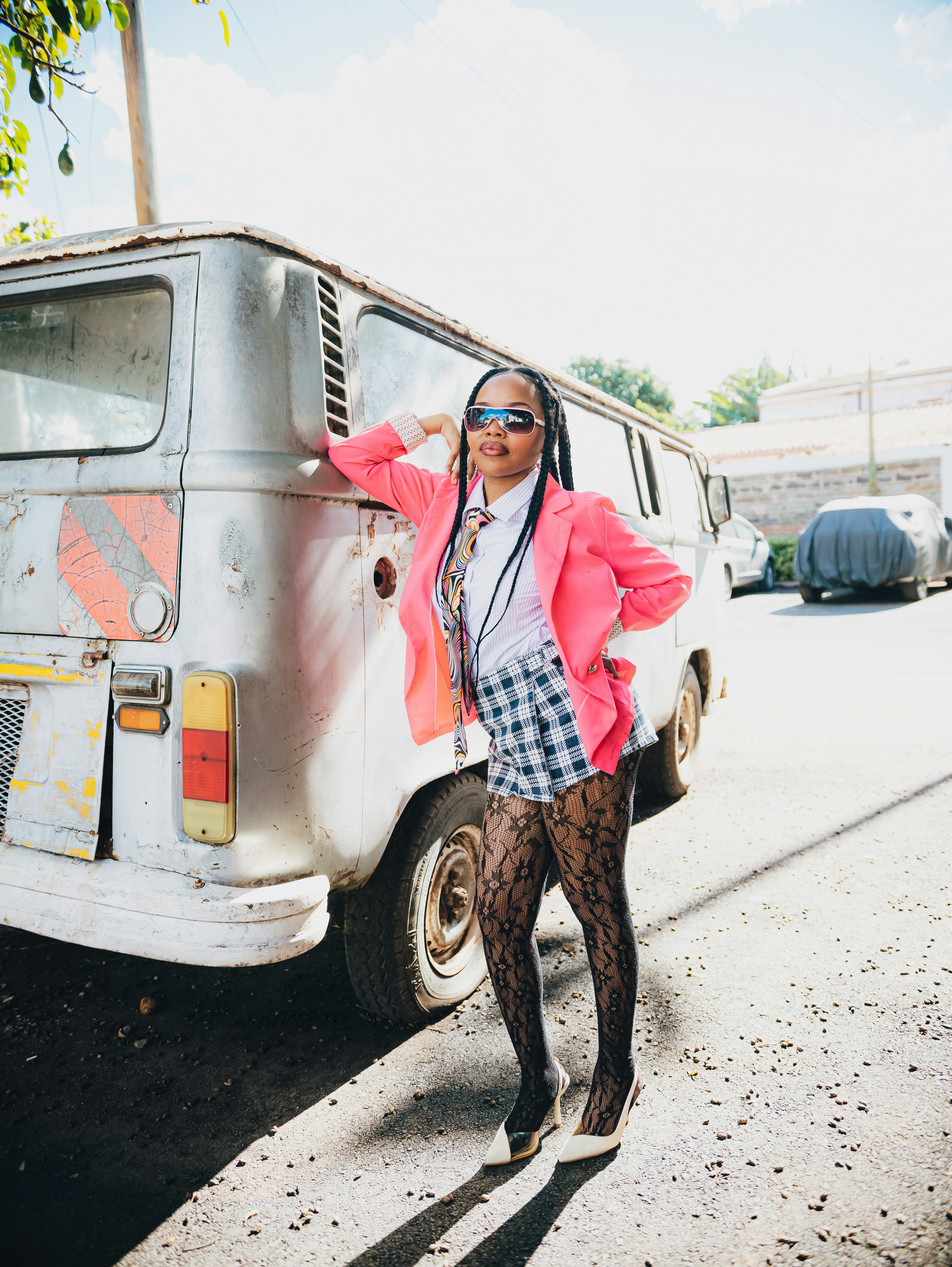 Mulher de blazer rosa e shorts xadrez apoiada na van.