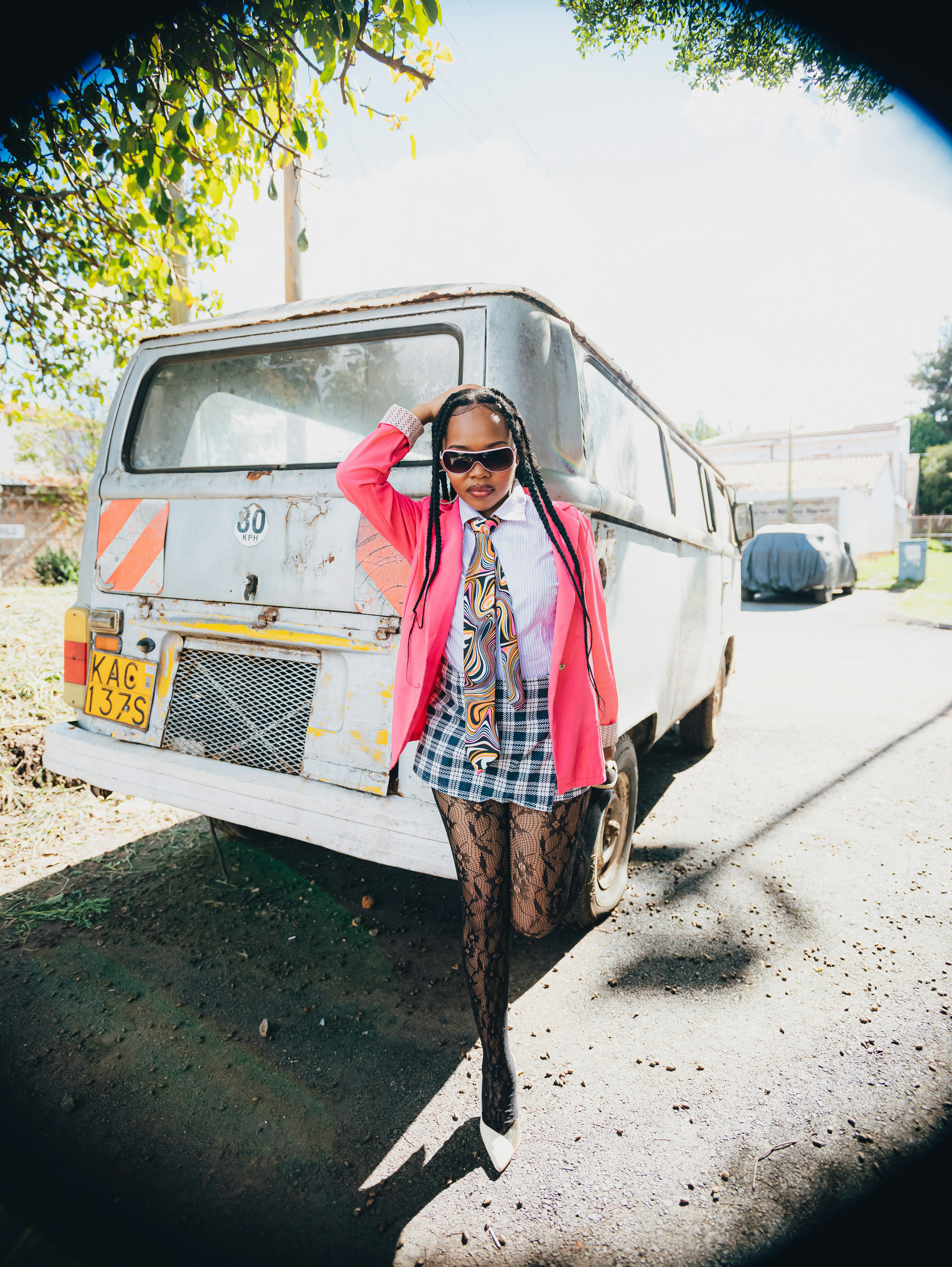 Mulher de blazer rosa e saia xadrez perto do ônibus velho