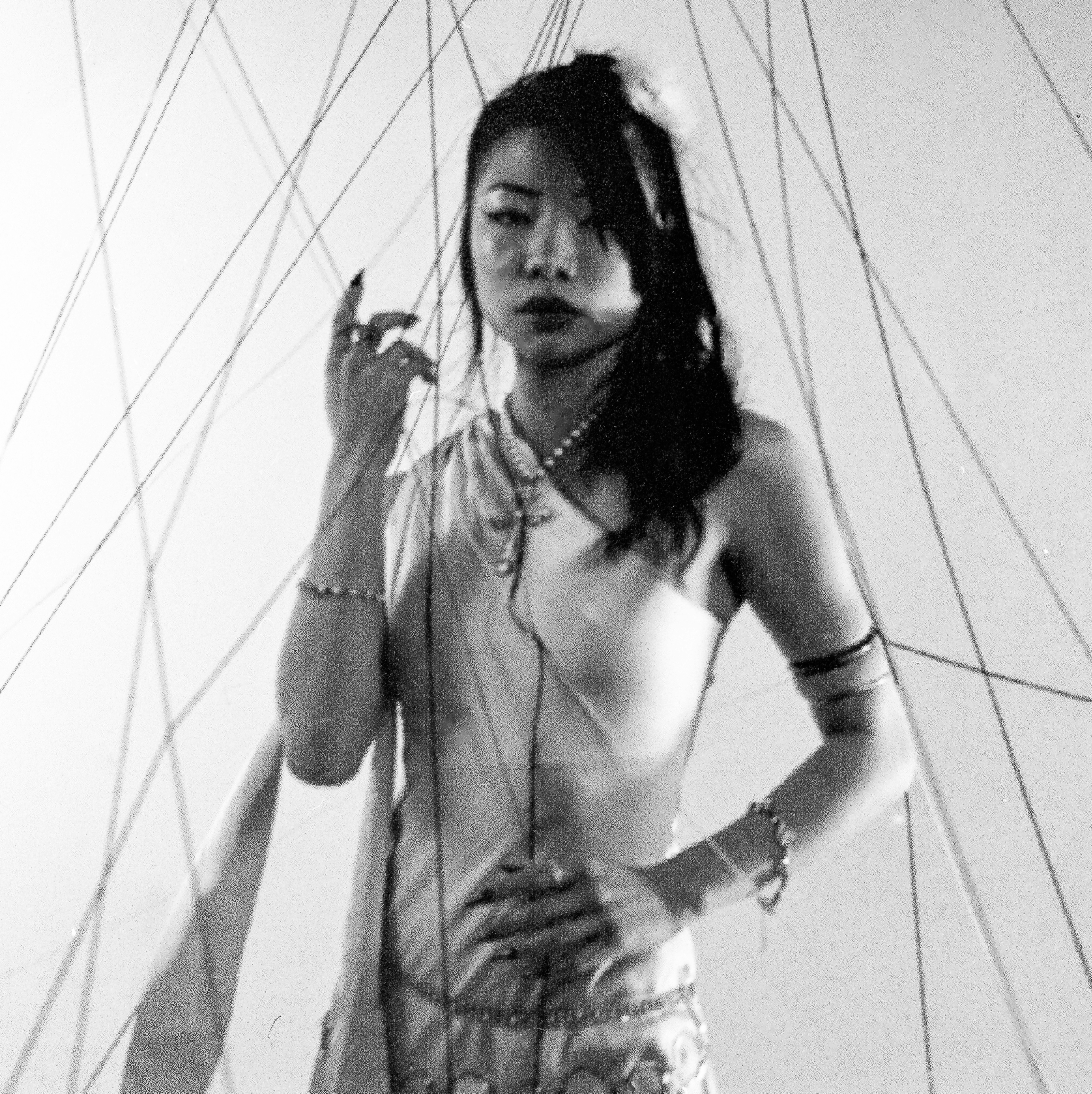Woman adorned with jewelry and threads in monochrome.