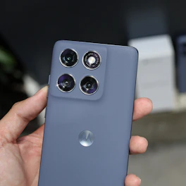 A hand holds a gray smartphone with four rear cameras.