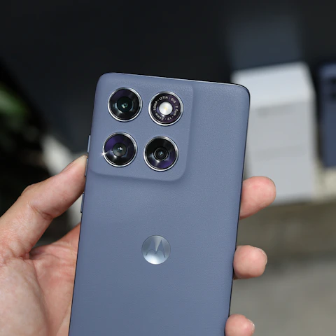 A hand holds a gray smartphone with four rear cameras.