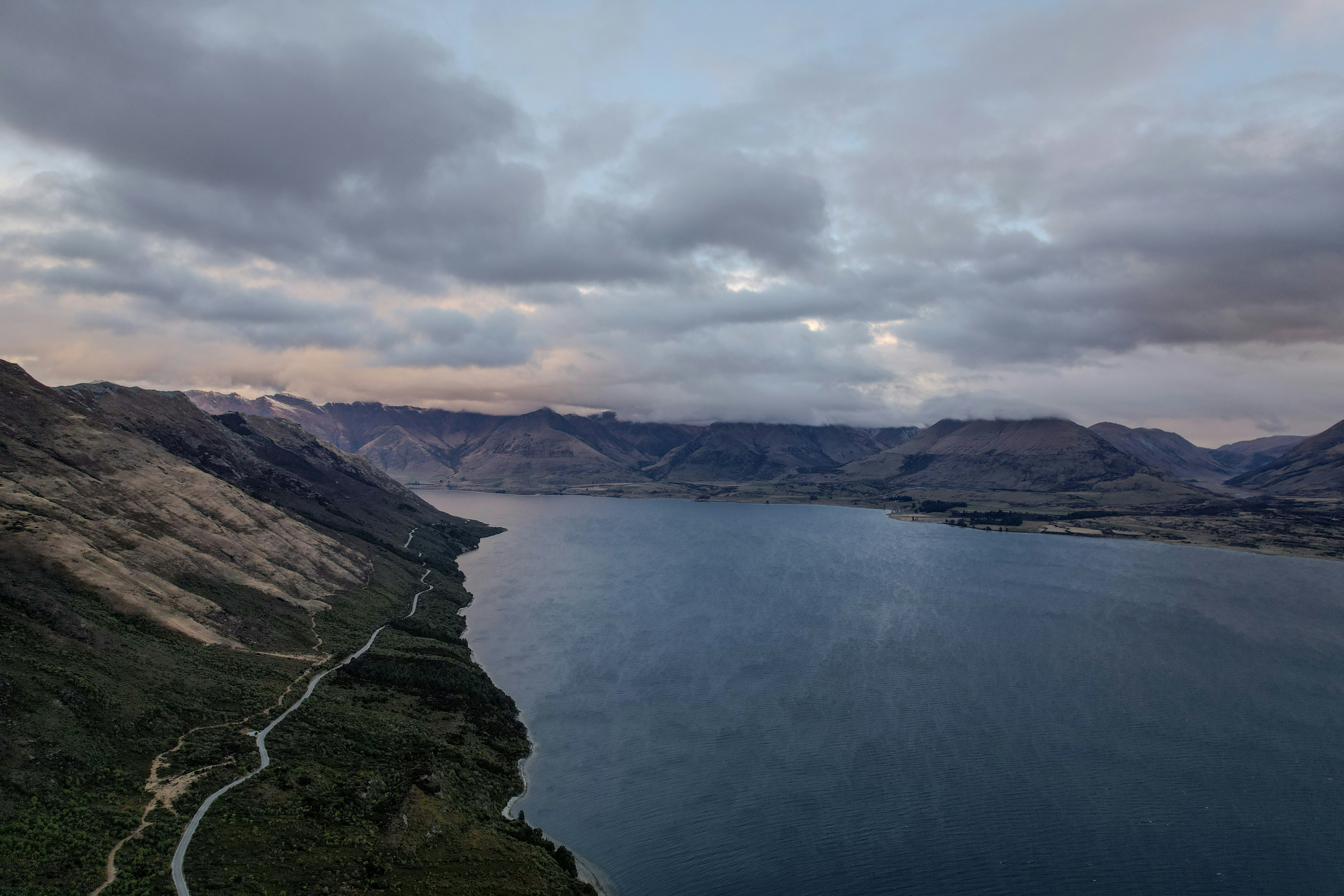 Uma estrada sinuosa ao lado de um grande lago com montanhas.