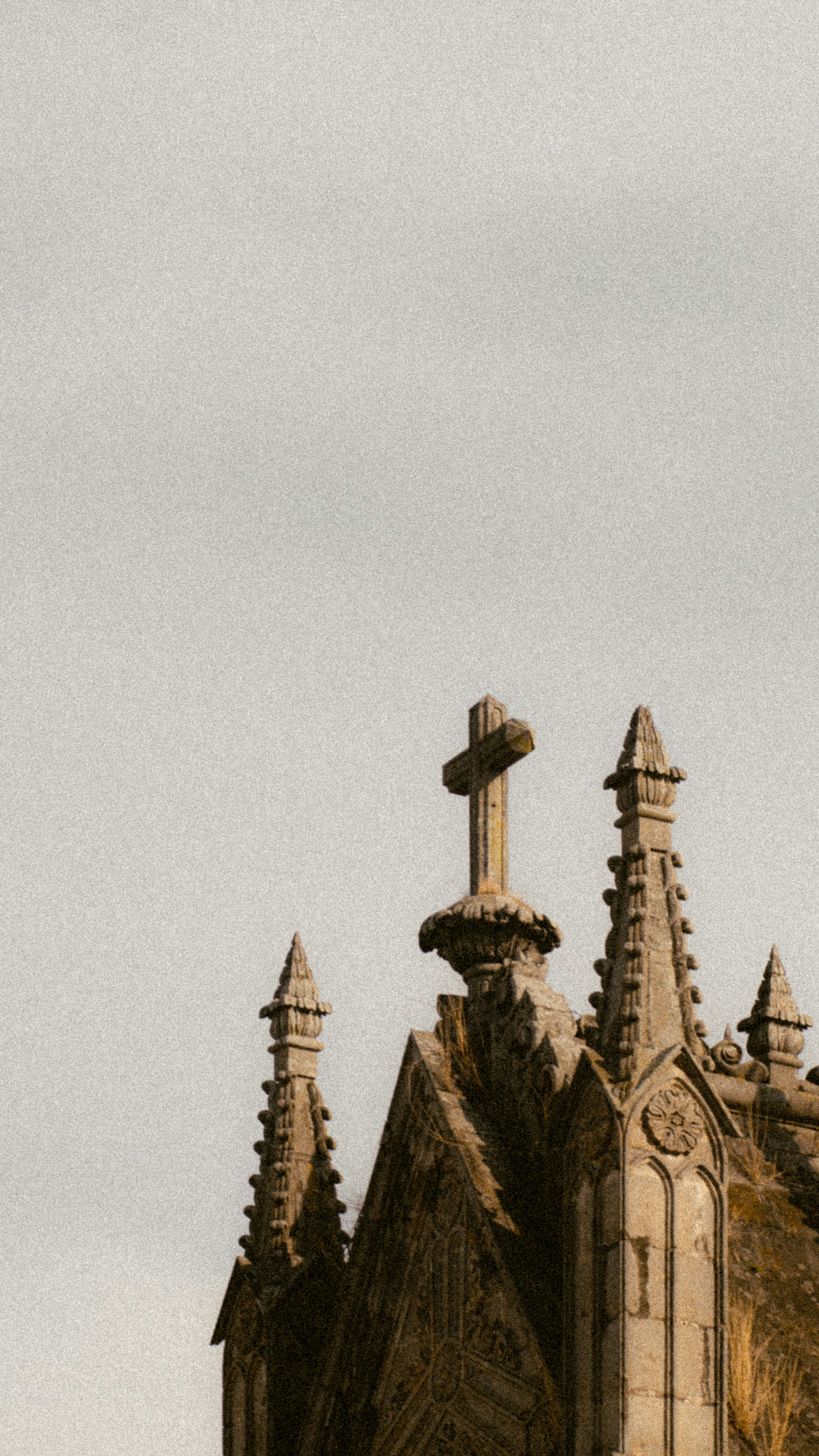 Gothic architecture with a cross against a pale sky.