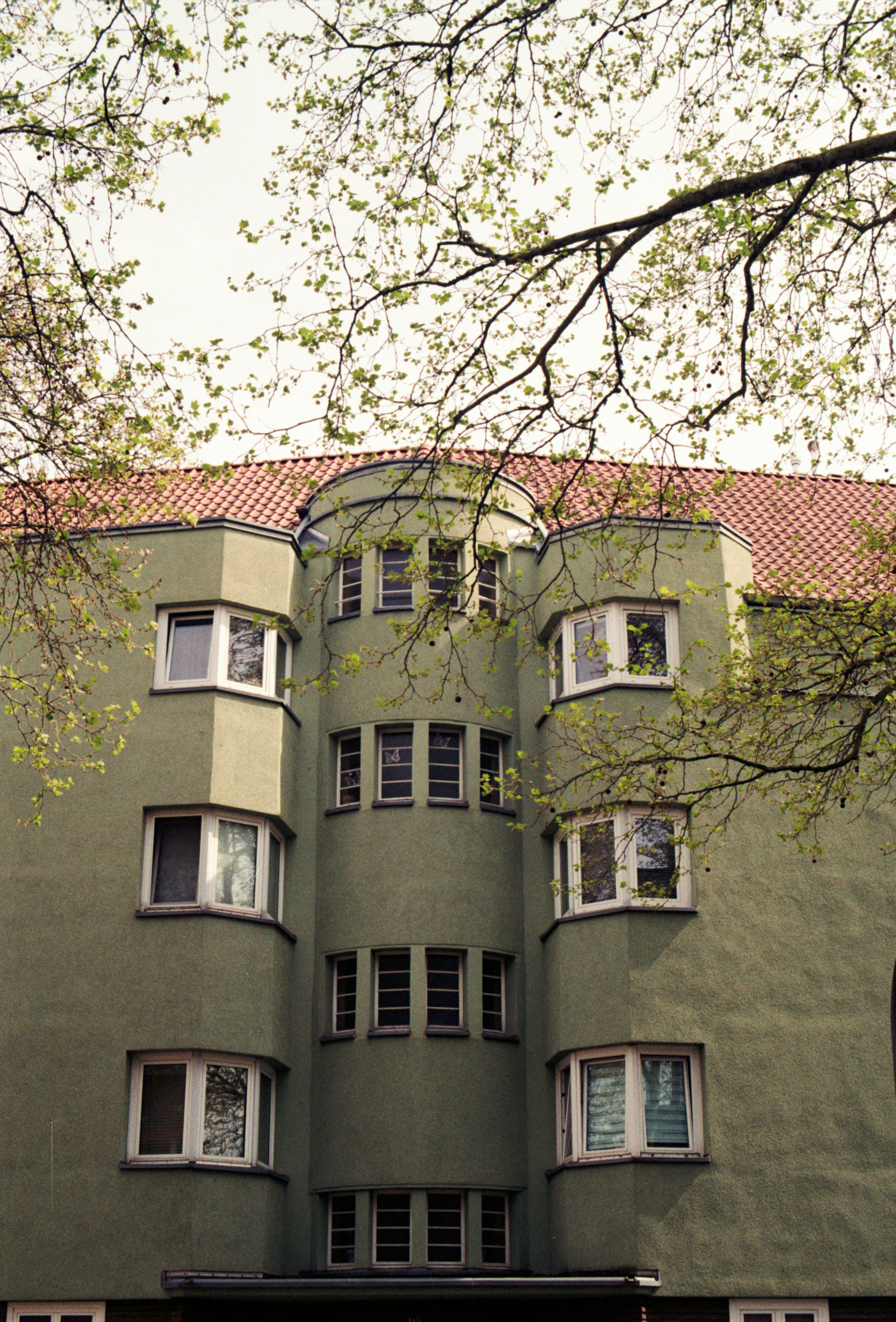 Edificio di appartamenti con facciata verde e tetto rosso tra gli alberi.