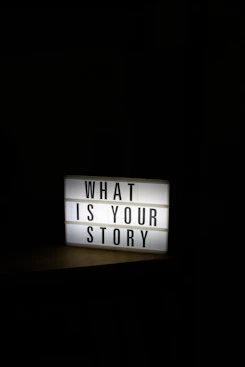 A glowing light box sign asks "what is your story".
