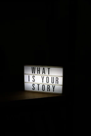 A glowing light box sign asks "what is your story"