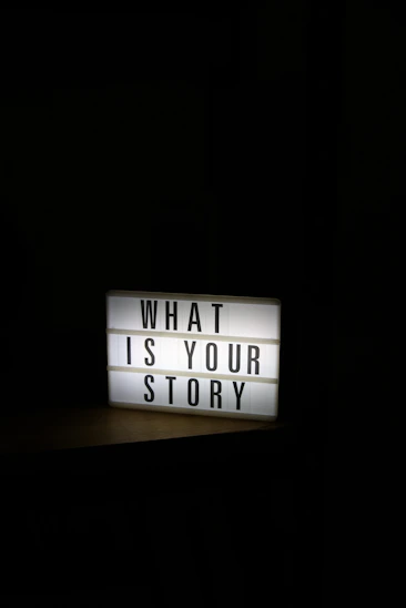 A glowing light box sign asks "what is your story"